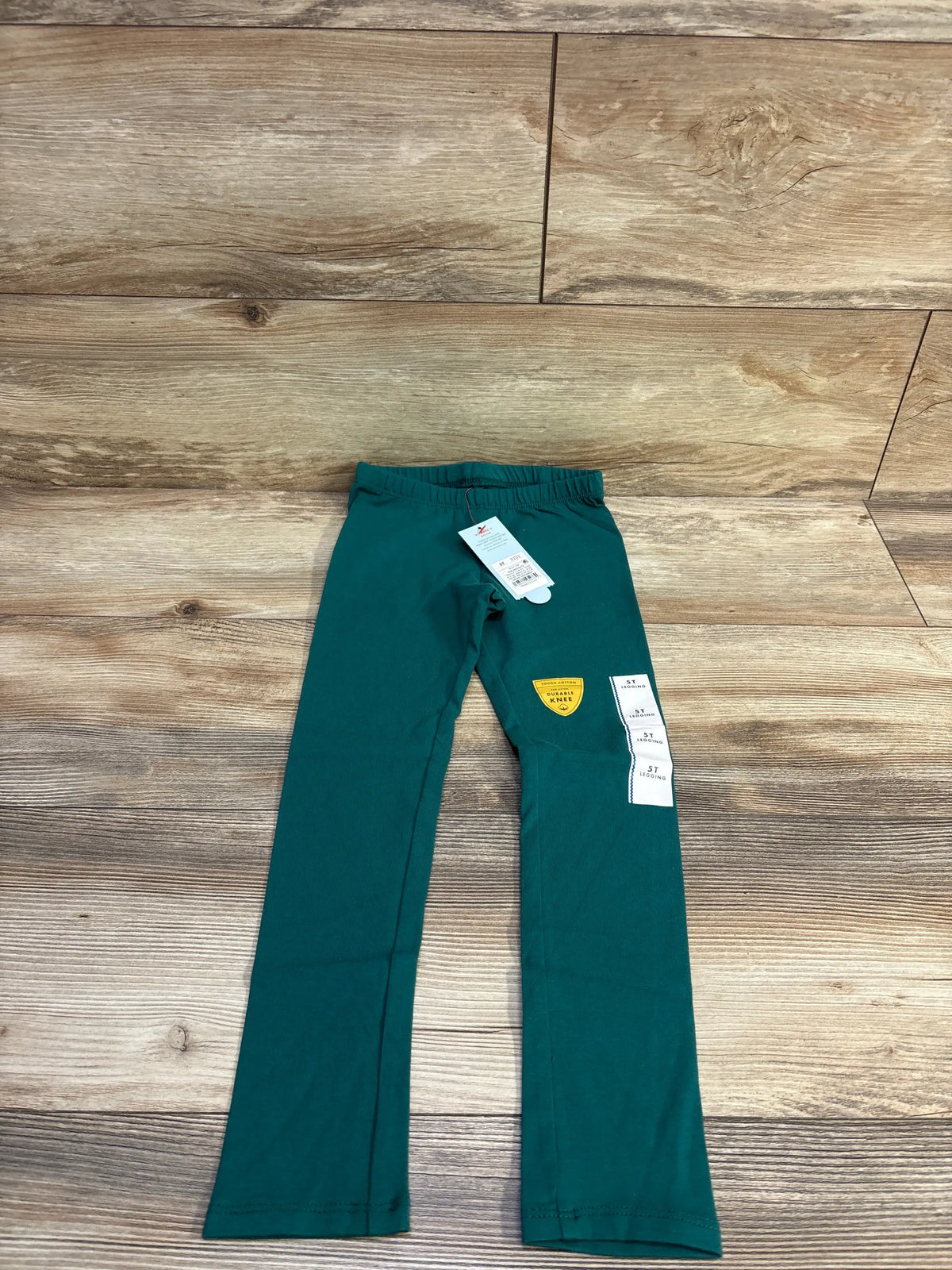 Flat lay of green Cat & Jack toddler leggings (size 5T) showing elastic waistband and attached tags on wood background