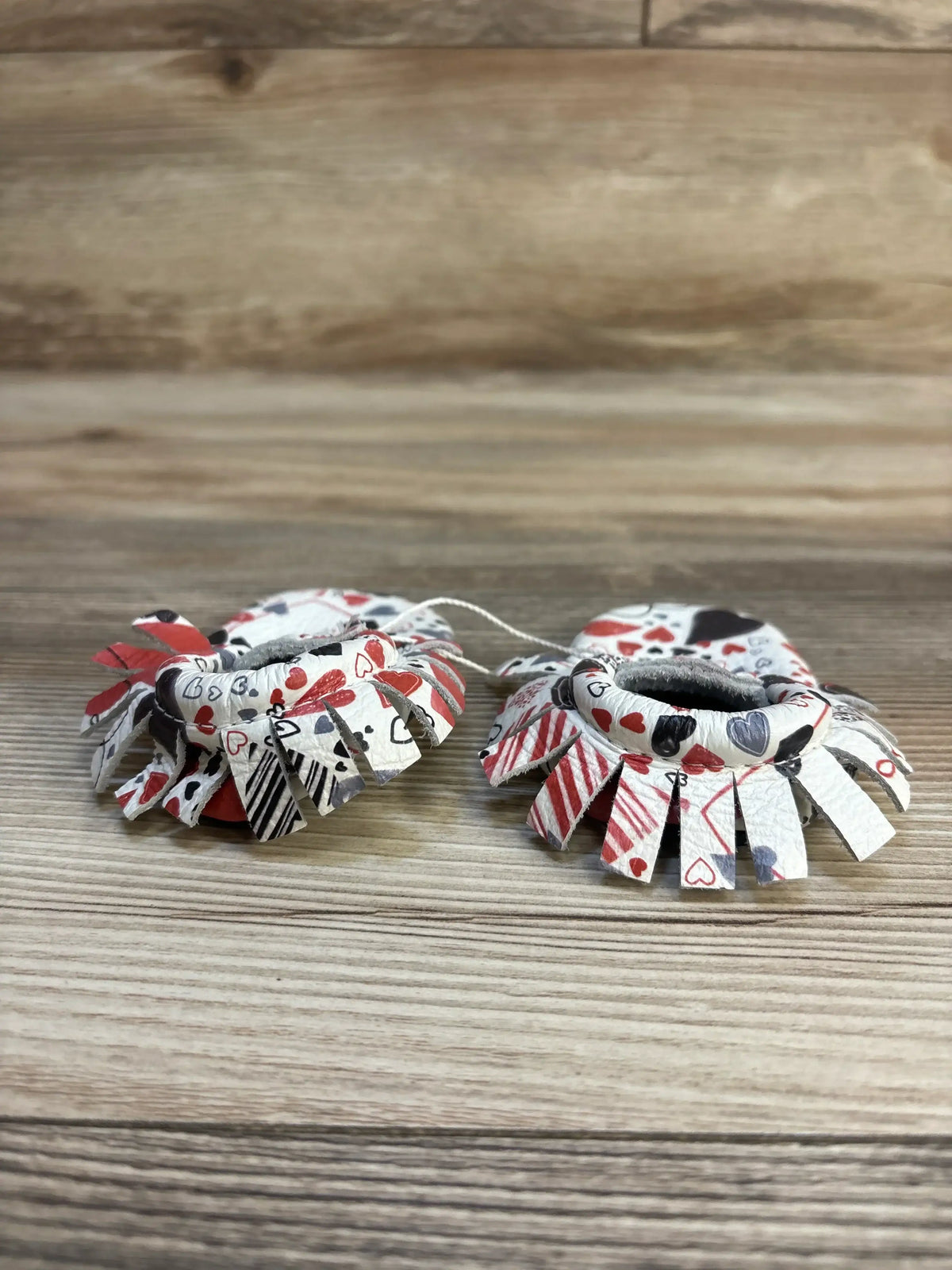 Heart print baby barefoot sandals with red, black, and white fringe details on wood background