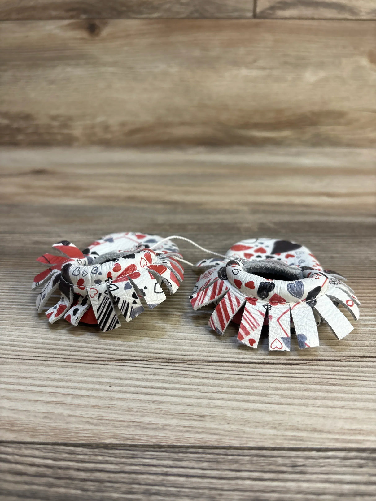 Heart print baby barefoot sandals with red, black, and white fringe details on wood background