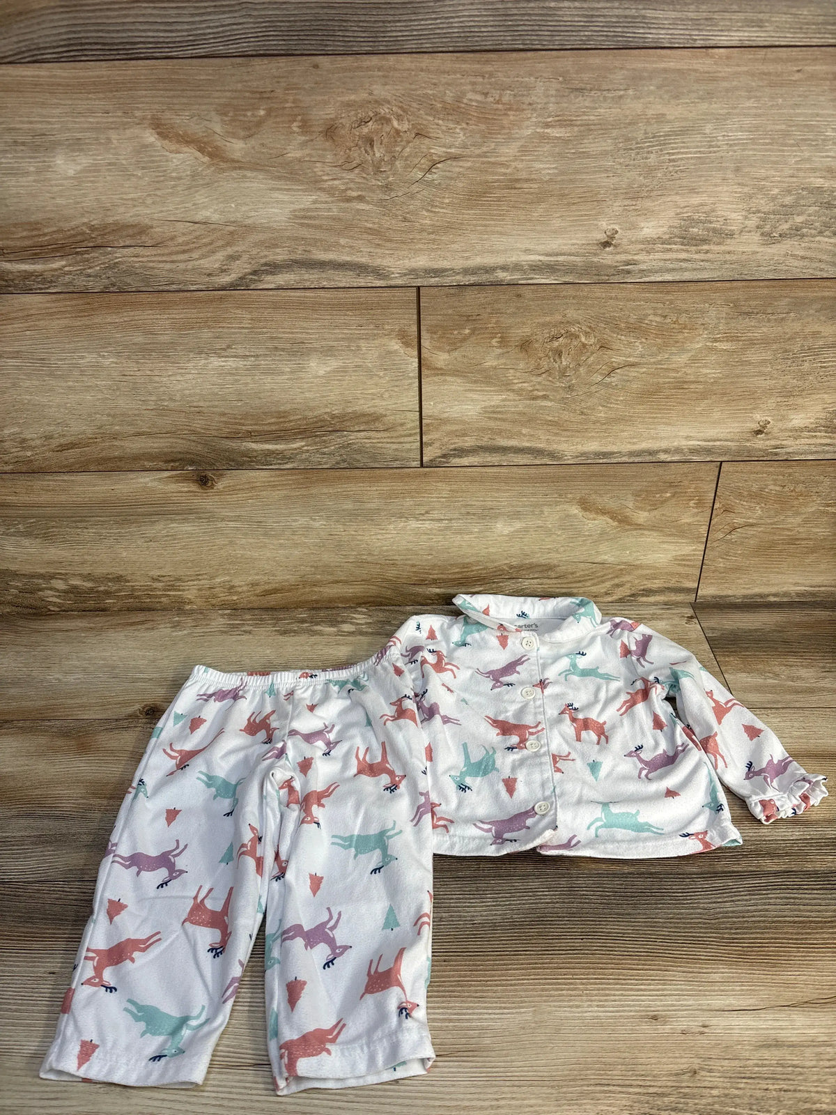 Flat lay of white 2-piece baby button-up top and elastic-waist pants with pastel deer print and ruffle cuffs, wood background