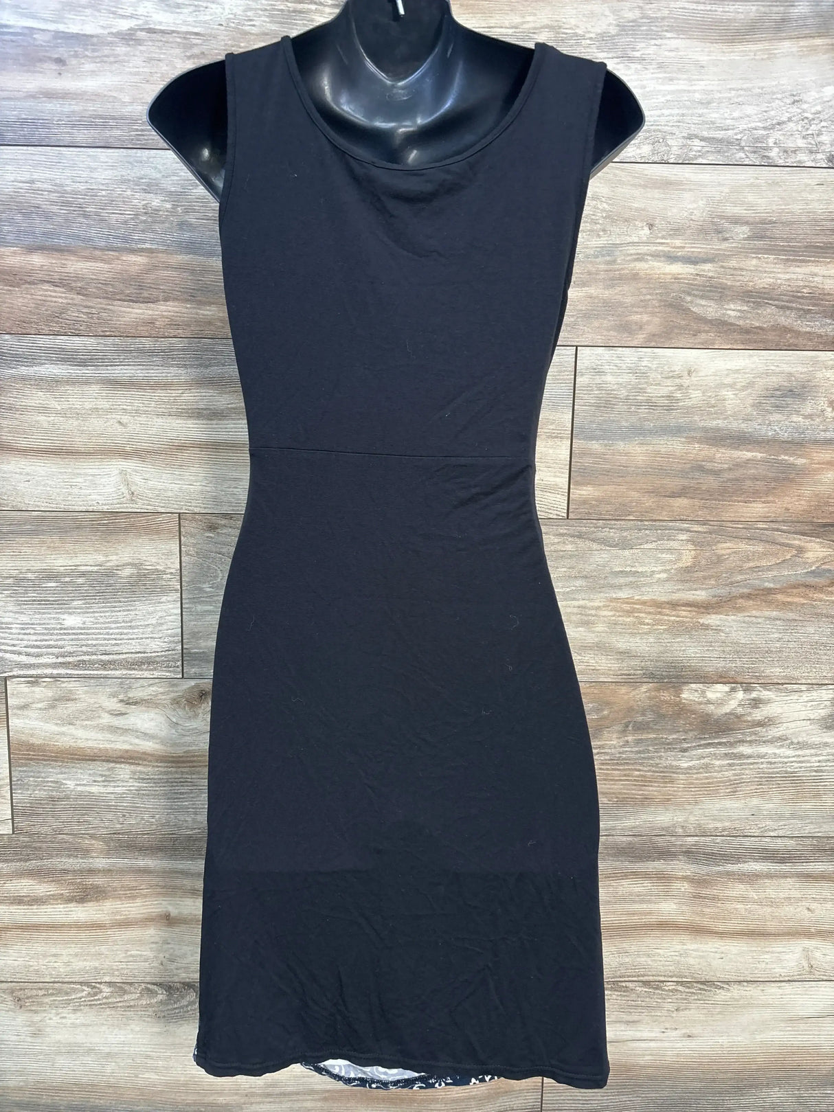 Front view of Kimi and Kai black maternity tank dress (size small) showing fitted waist seam and midi length on wood plank background