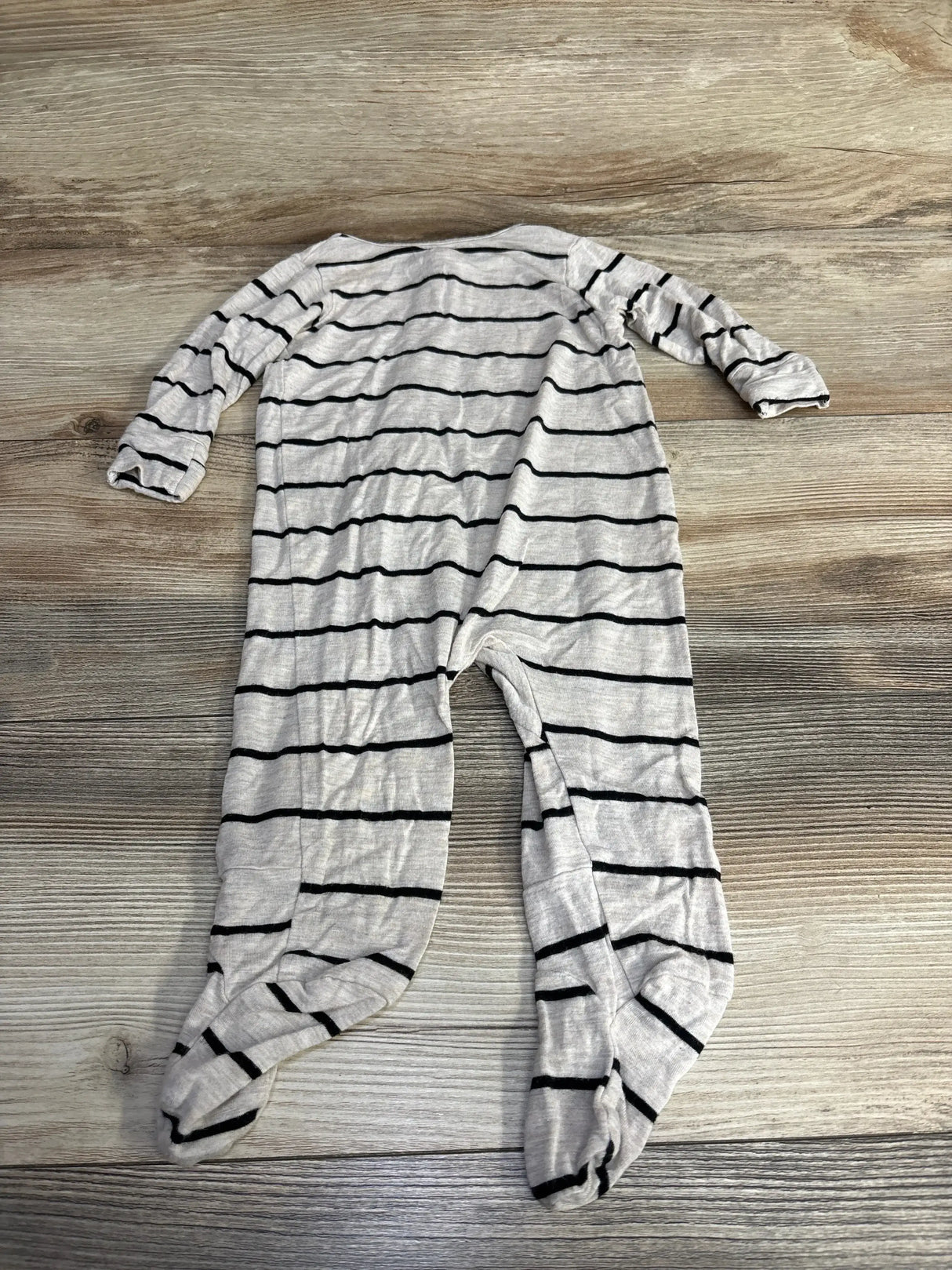 Flat lay of oatmeal grey striped baby footie (3–6 months) showcasing long sleeves and enclosed feet on a wood floor background