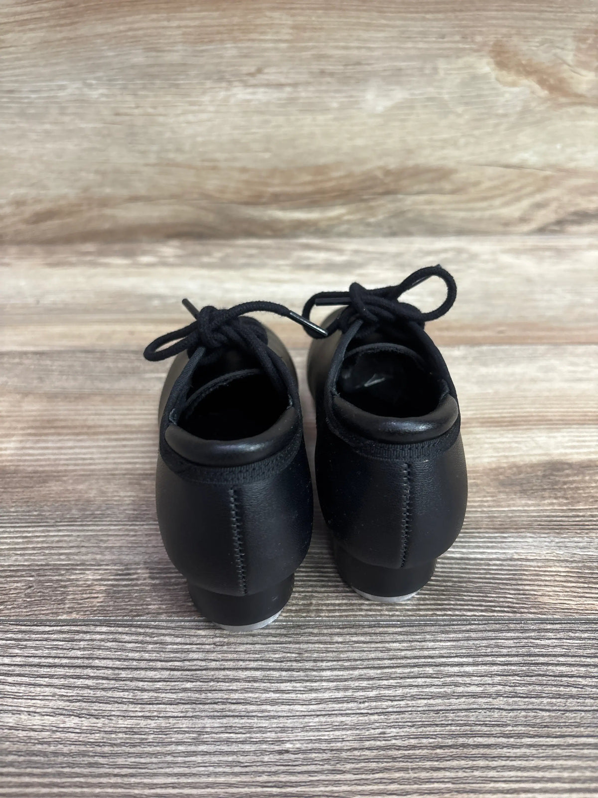 Rear view of Theatricals Footwear black lace-up tap shoes, size 9.5C, showing tied laces and heel taps on a wood-look floor