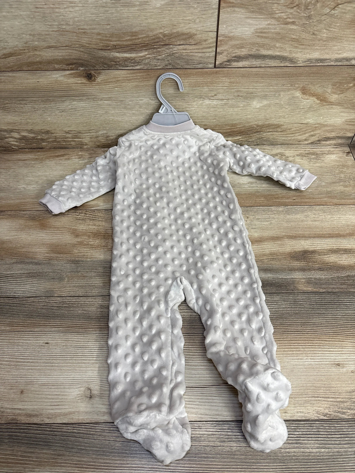 Soft white textured baby sleeper with feet on wooden floor, new with hanger at children's resale store