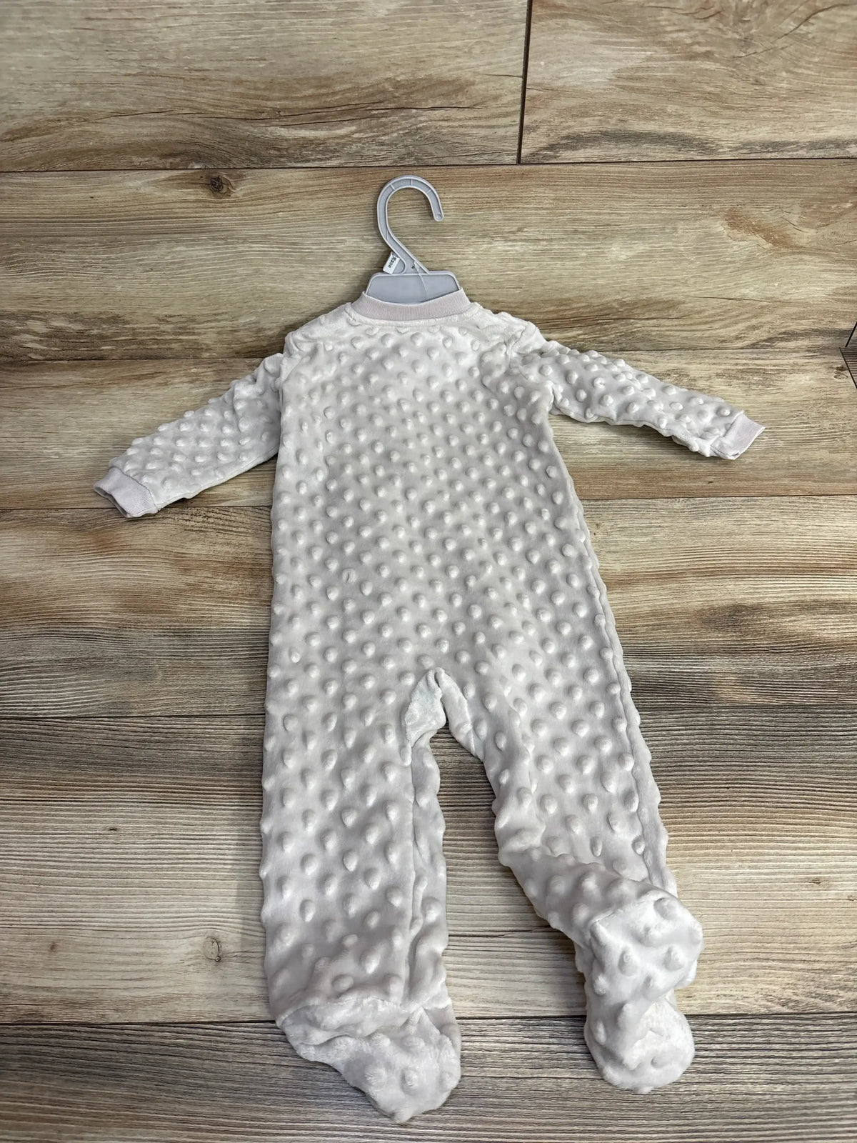 Soft white textured baby sleeper with feet on wooden floor, new with hanger at children's resale store