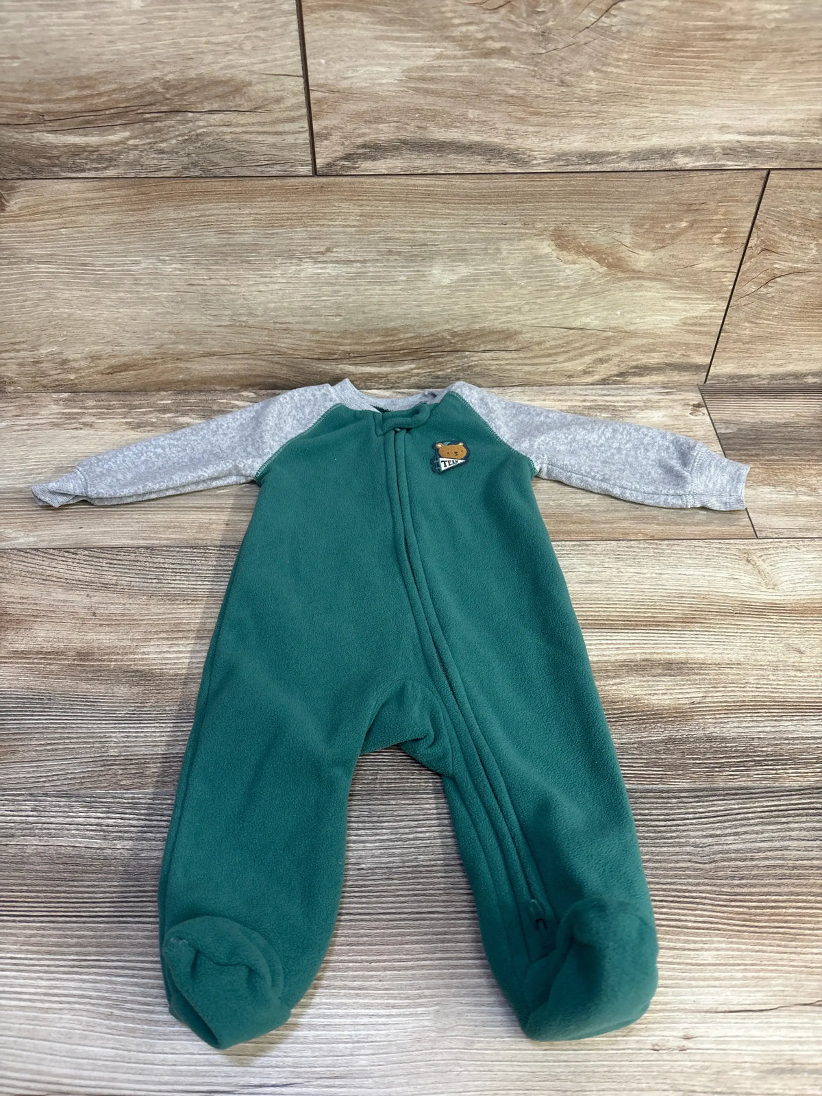Front flat lay of Carter's green footed sleeper with gray heather sleeves, small bear patch, front zipper on wood background