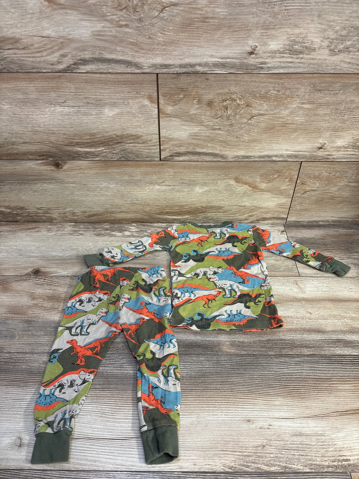 Flat lay of Carter’s two-piece green dinosaur-print pajama set with long-sleeve top and pants on a wood-look floor
