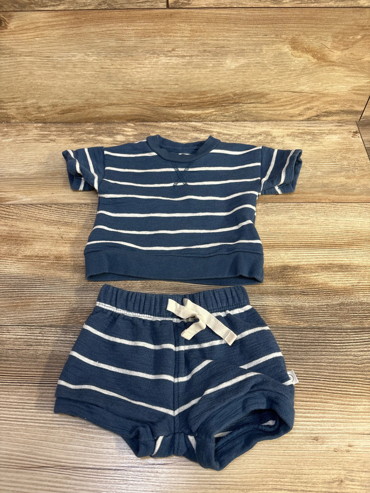 Top view of Little Planet organic striped shirt and shorts set showcasing short sleeves and elastic-waist shorts on wood