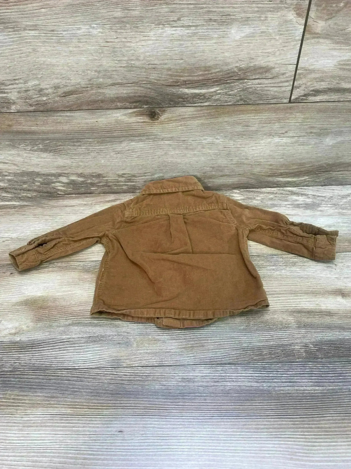 Back view of brown corduroy toddler button-up shirt size 12m showing back pleat and sleeves on light wood background
