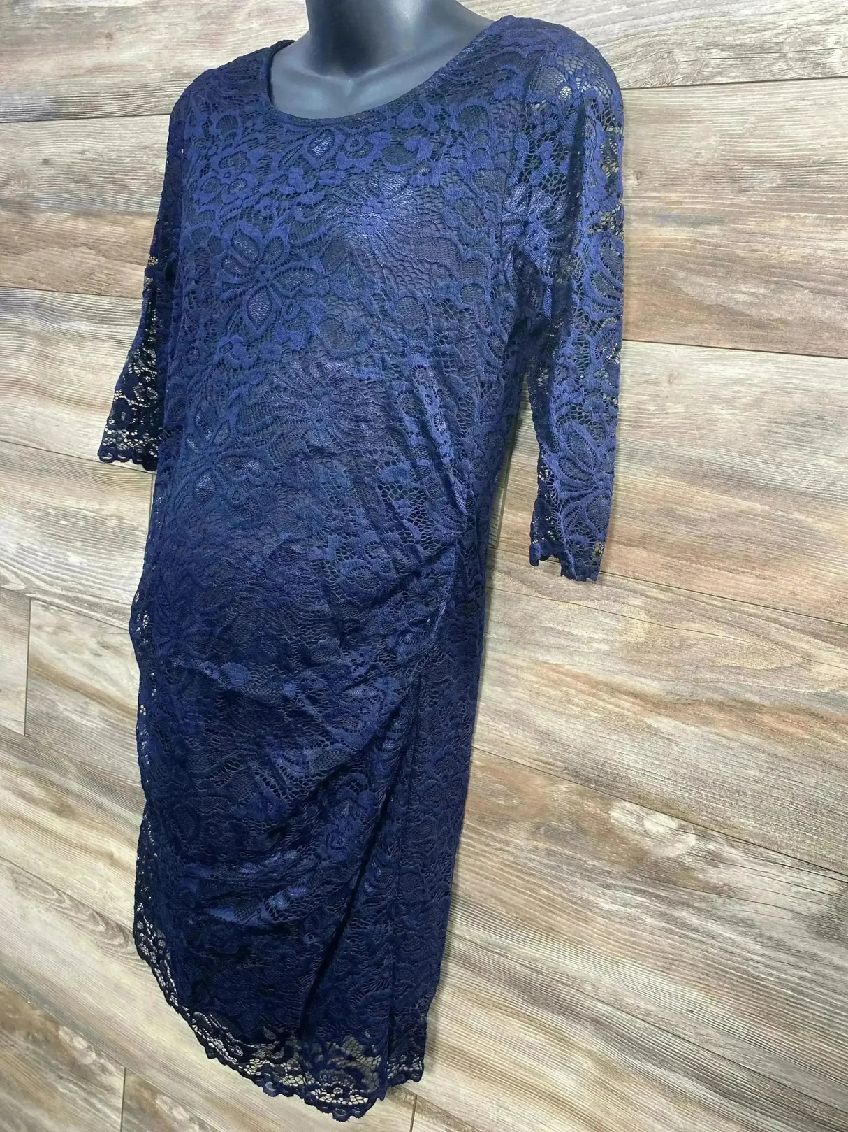 Front view of navy fitted 3/4-sleeve lace maternity dress showcasing floral lace overlay and scalloped hem with wood plank background