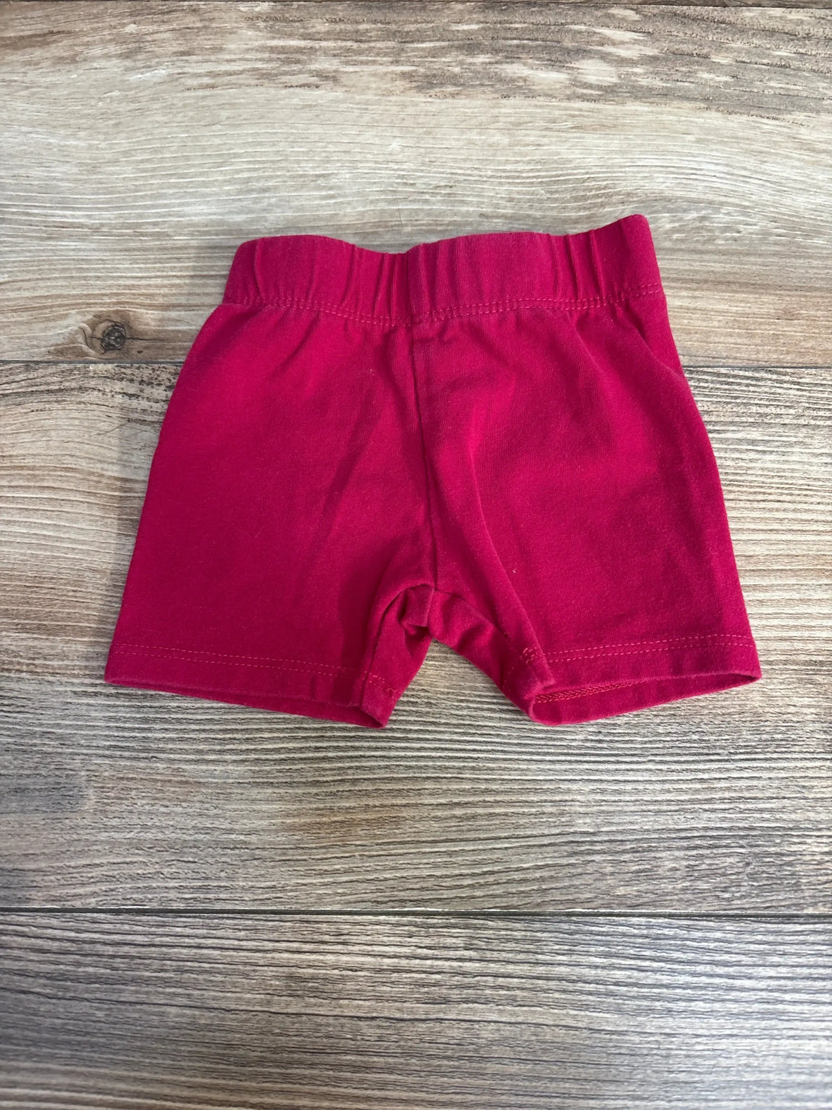 Front flat lay of pink baby bike shorts size 3-6 months showcasing elastic waistband and short legs on wooden background