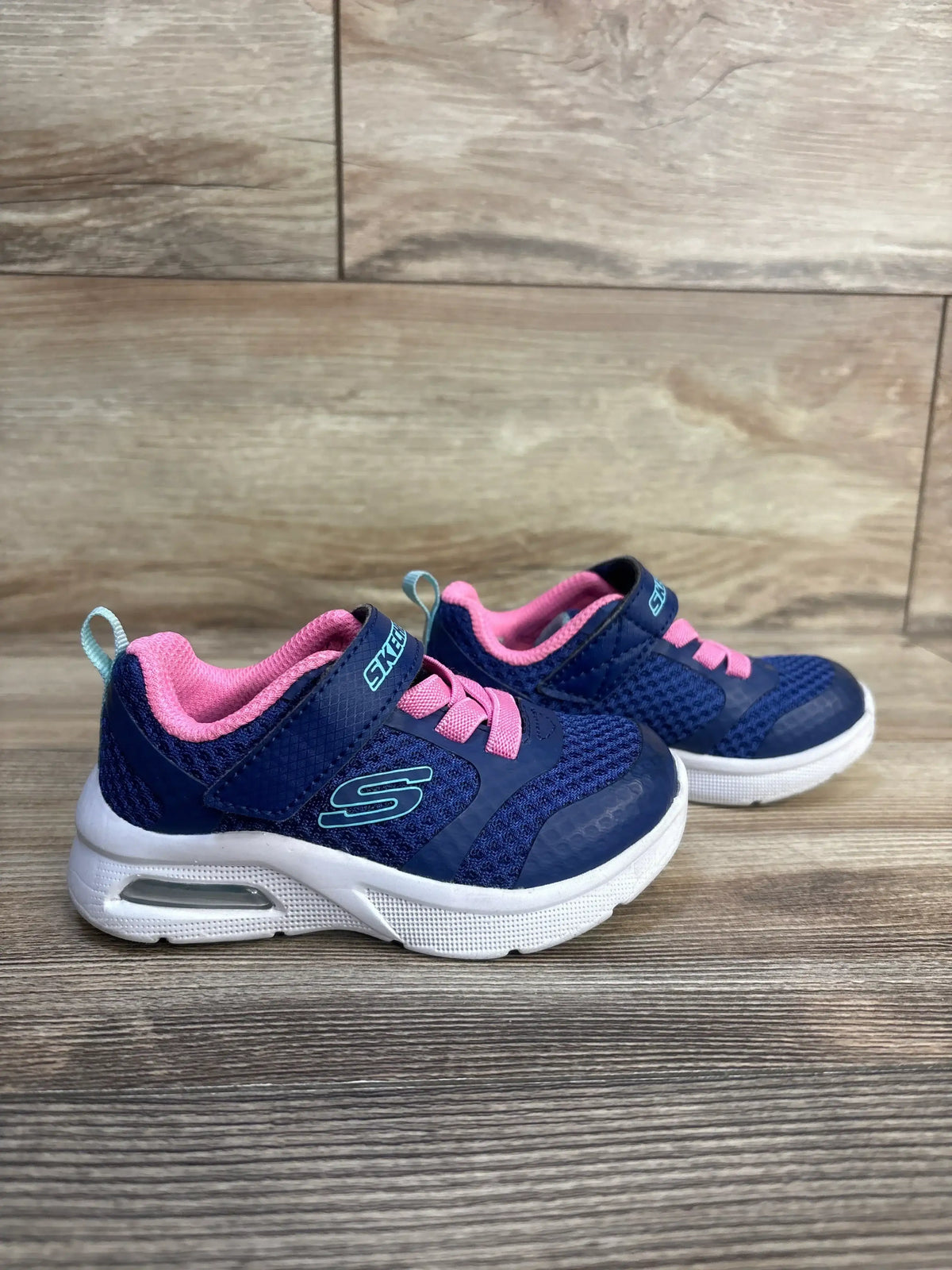 Navy blue and pink Skechers toddler sneakers with velcro straps, white soles, and air cushion detail on wood floor