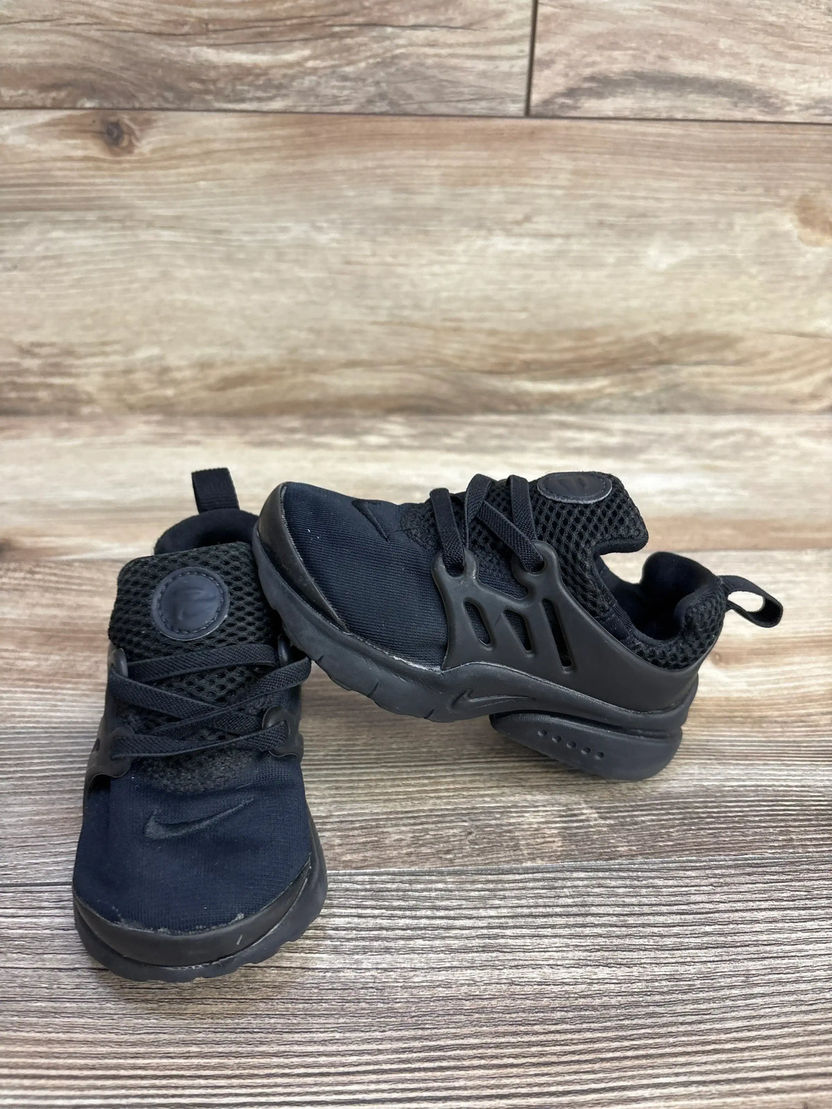 Black toddler Nike sneakers on wood floor, mesh and synthetic design, side view