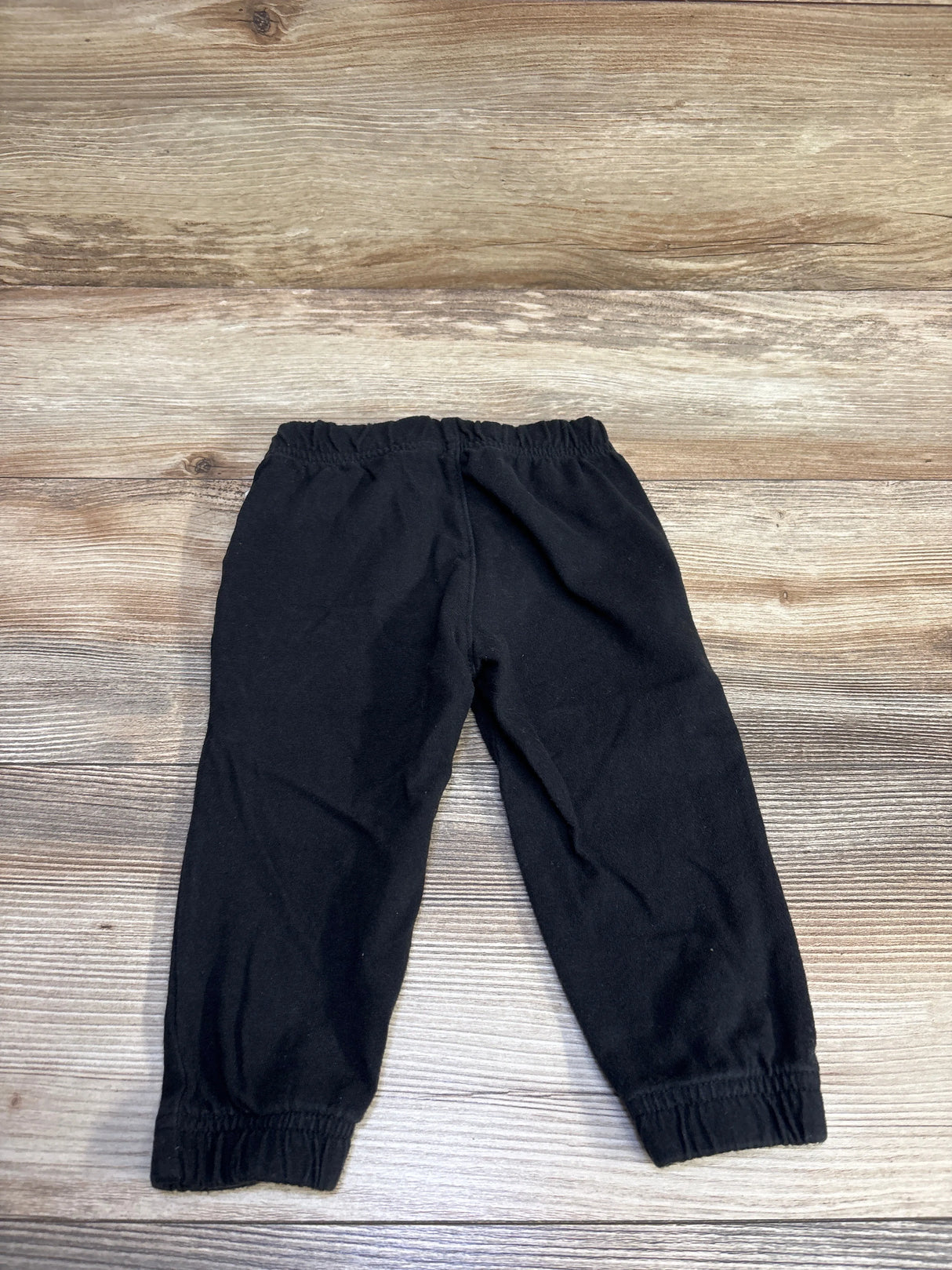 Flat lay of Baby Gap black toddler joggers (12–18 months) showcasing elastic waistband and cuffed ankles on wood background