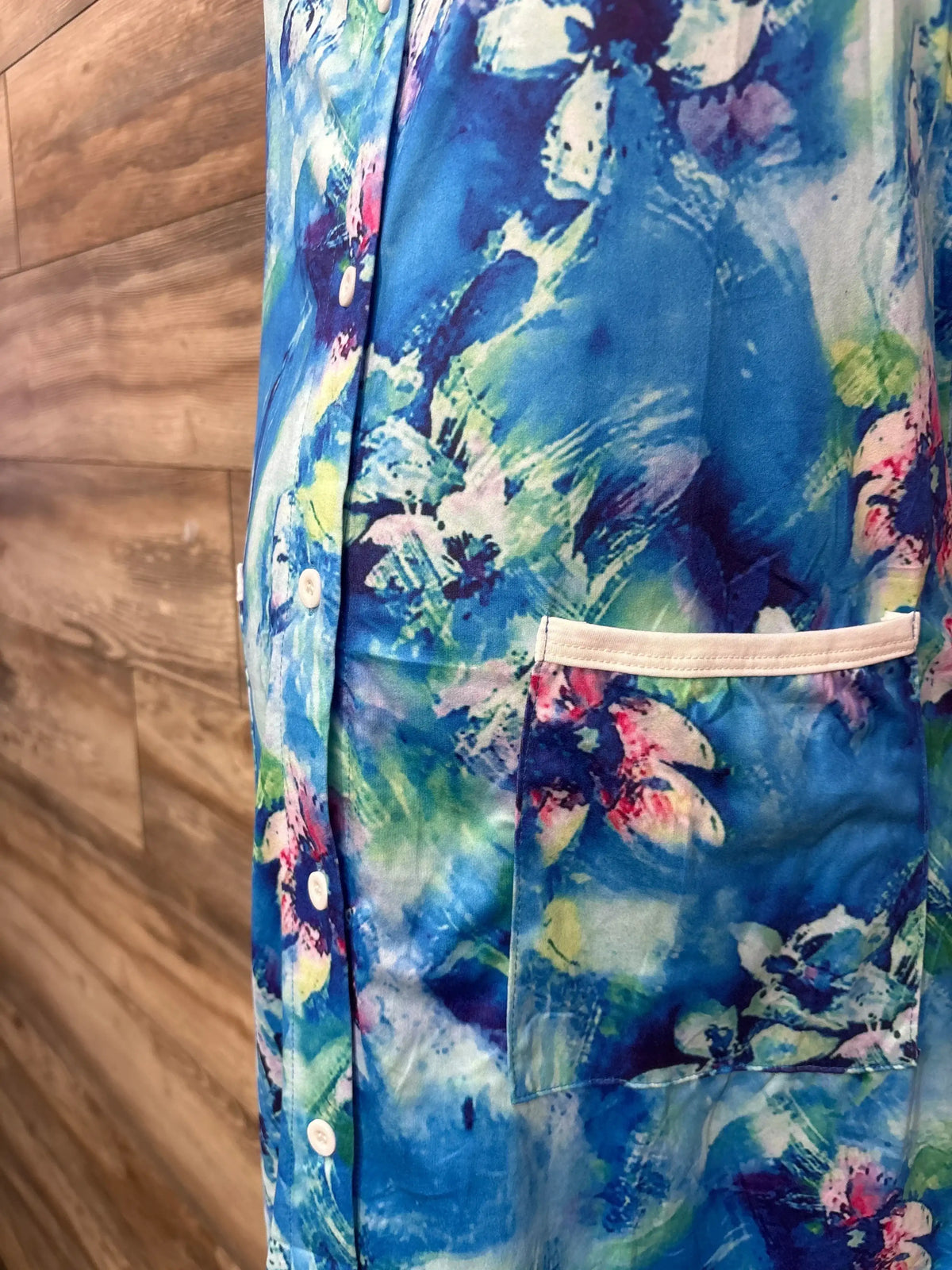 Side close-up of blue floral maternity tank dress with button placket and white-trim patch pocket on wood background