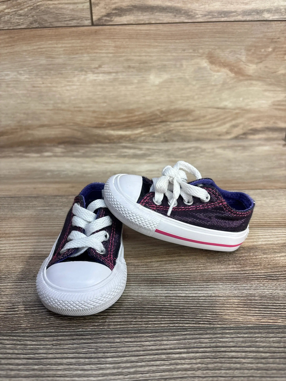 Pair of purple canvas toddler sneakers with white laces on wood floor