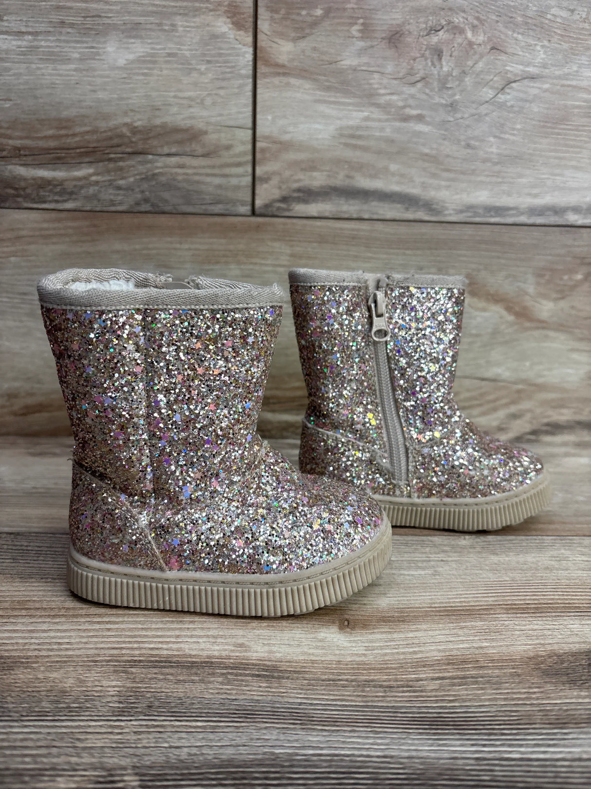 Pair of glittery toddler boots with side zipper on wooden floor background