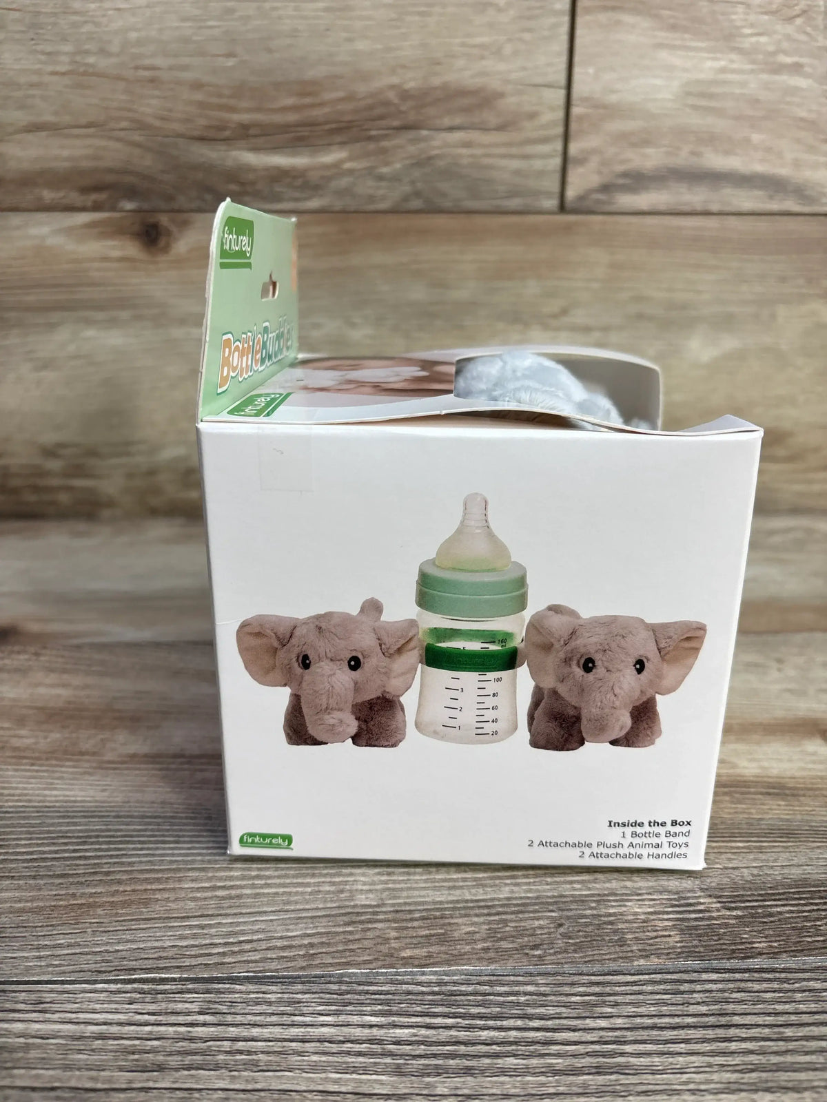 Front of Bottle Buddies elephant starter kit box showing two gray elephant plush toys and baby bottle on wooden background