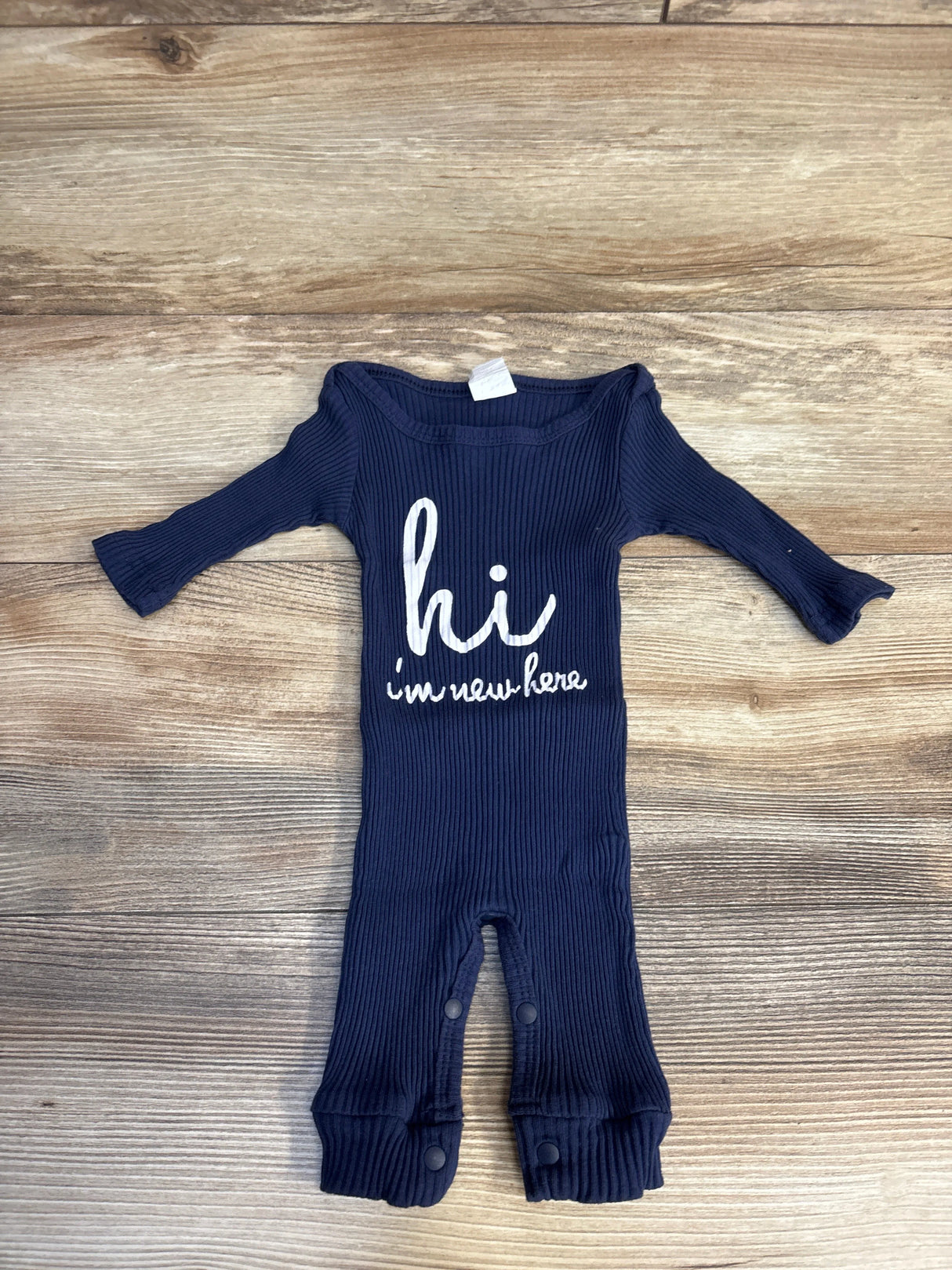 Navy blue ribbed baby onesie with 'hi i'm new here' print, long sleeves, snap closures, on wood floor