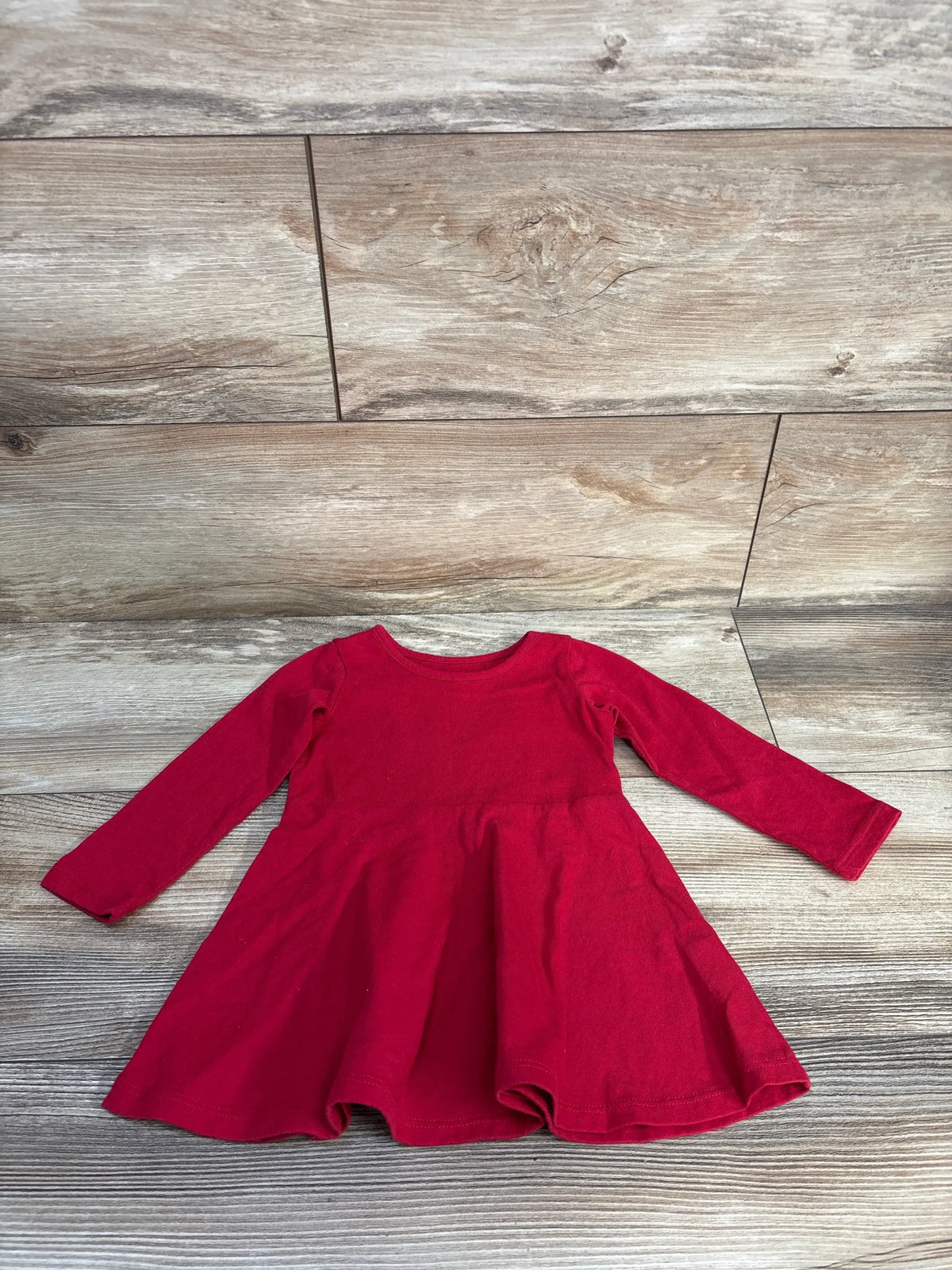 Front view of Children’s Place red long sleeve dress showcasing its gathered waist and flared skirt on a wood floor