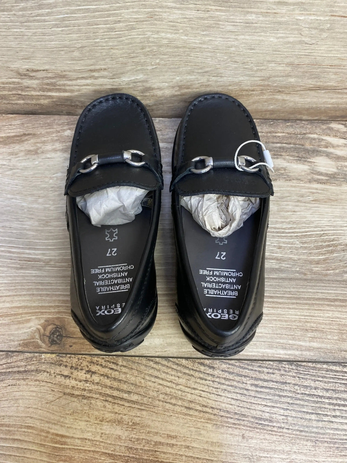 Top-down view of GEOX black toddler loafers (size 10 C) showcasing silver chain bit across vamp on wood background