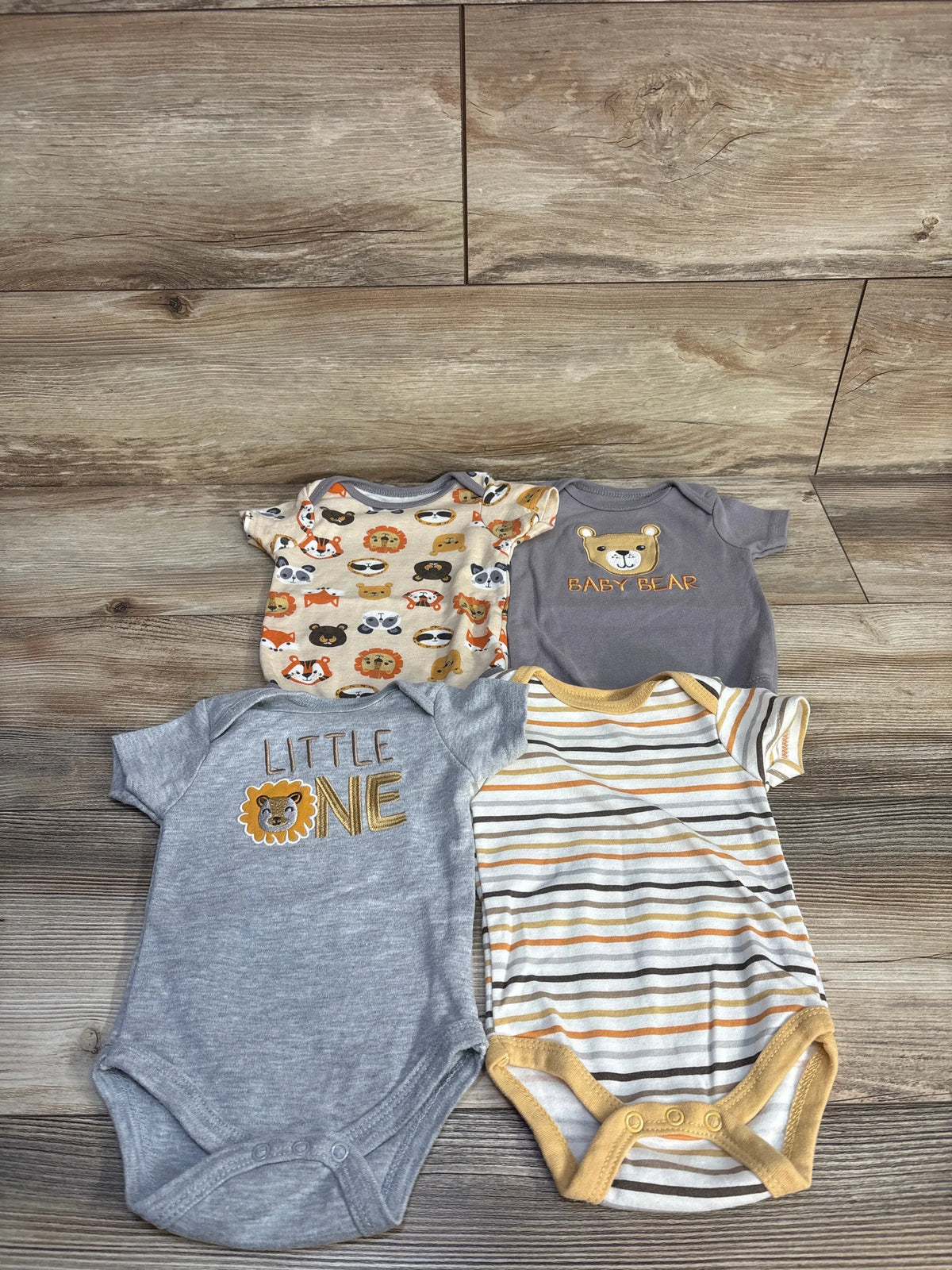 Top-down view of Chick Pea four-piece baby bodysuit set with animal graphics, BABY BEAR and LITTLE ONE text, on a wood floor