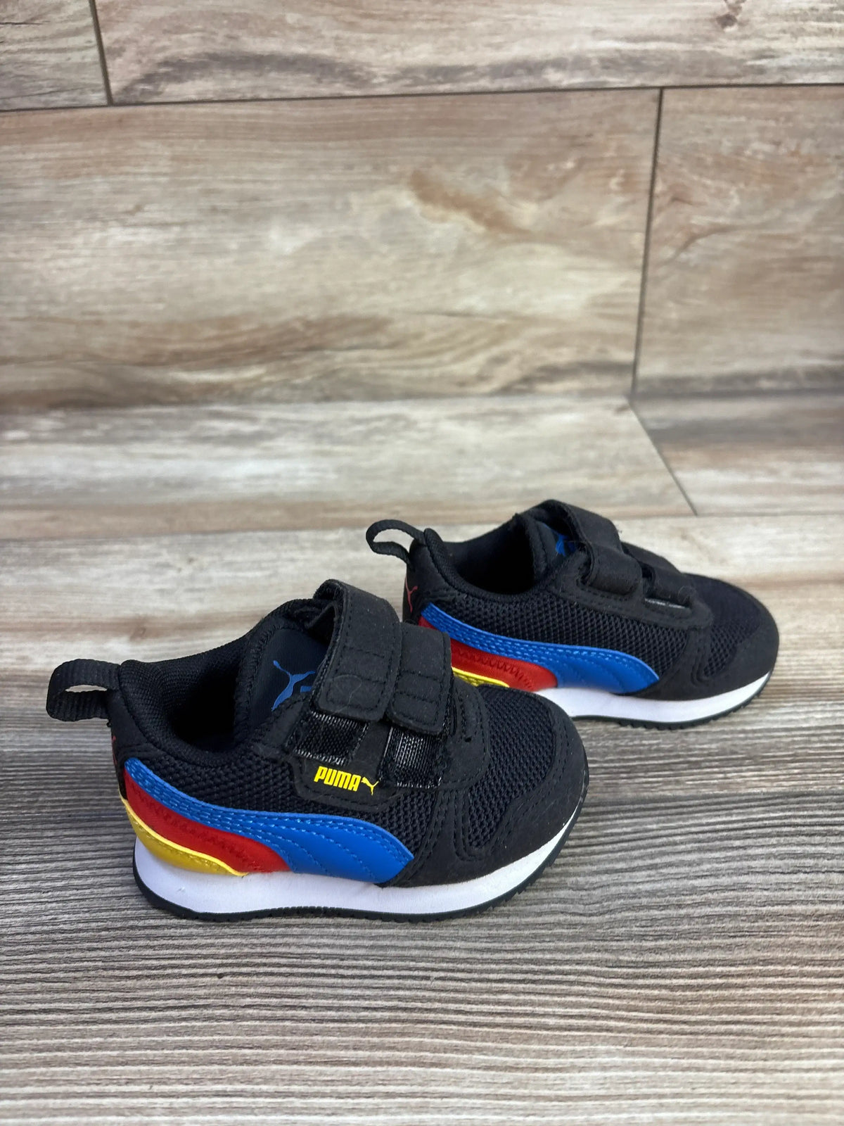 Front and side view of Puma R78 double strap sneakers in black with colorful accents and white cushioned soles on wood-look flooring