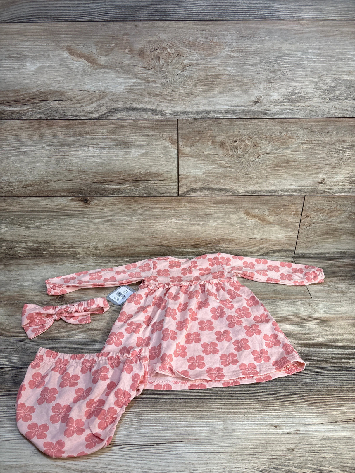 Pink floral baby outfit with long-sleeve top, bloomers, and headband on wood floor