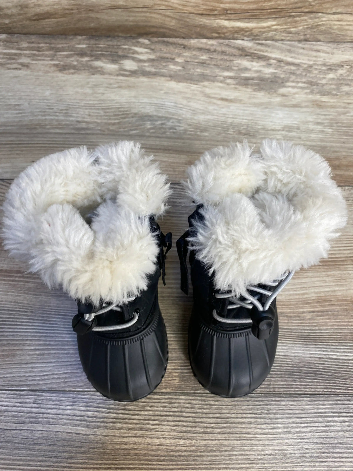 Top down view of Native Jimmy winter boots size 5C showcasing white faux fur cuff and black rubber soles on wood floor