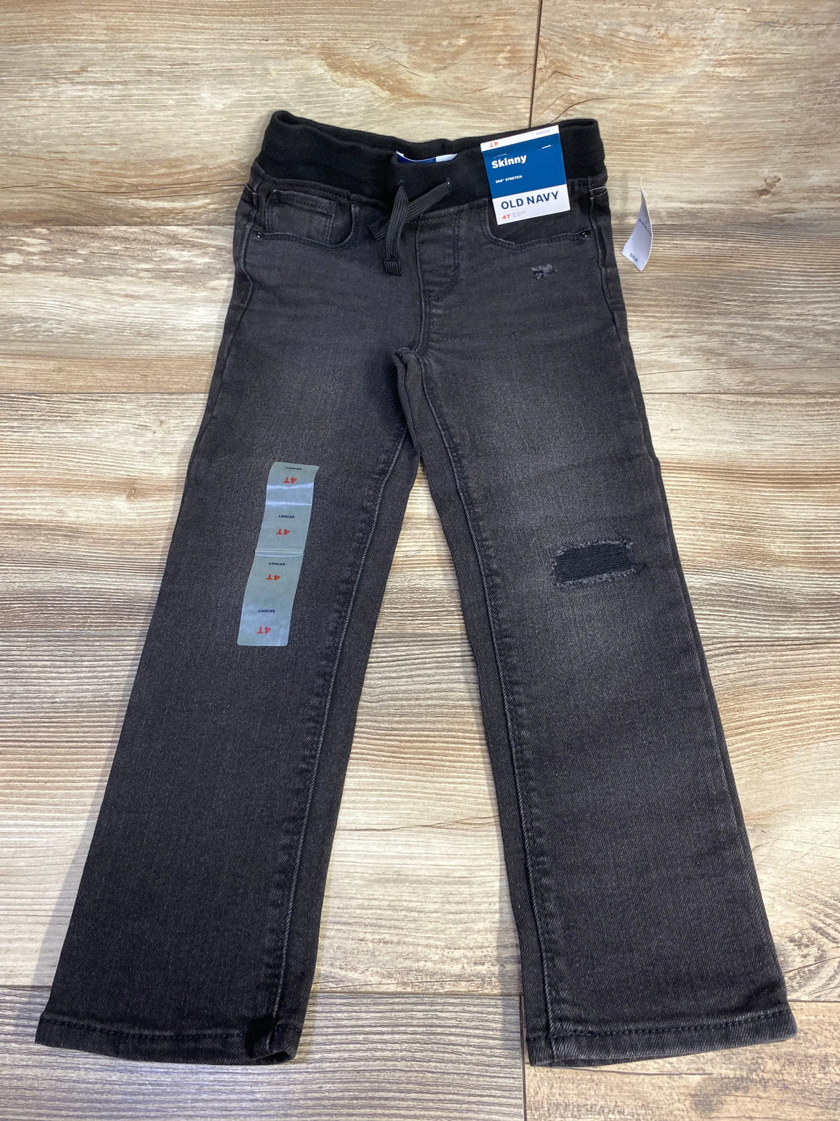 Black Old Navy kids skinny jeans with elastic waistband and patch detail, laid on wood floor