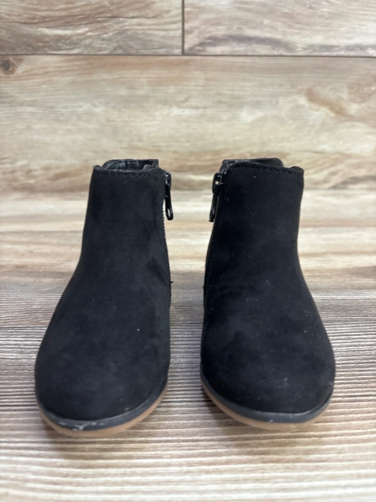 Pair of black toddler suede ankle boots with side zippers on wooden floor