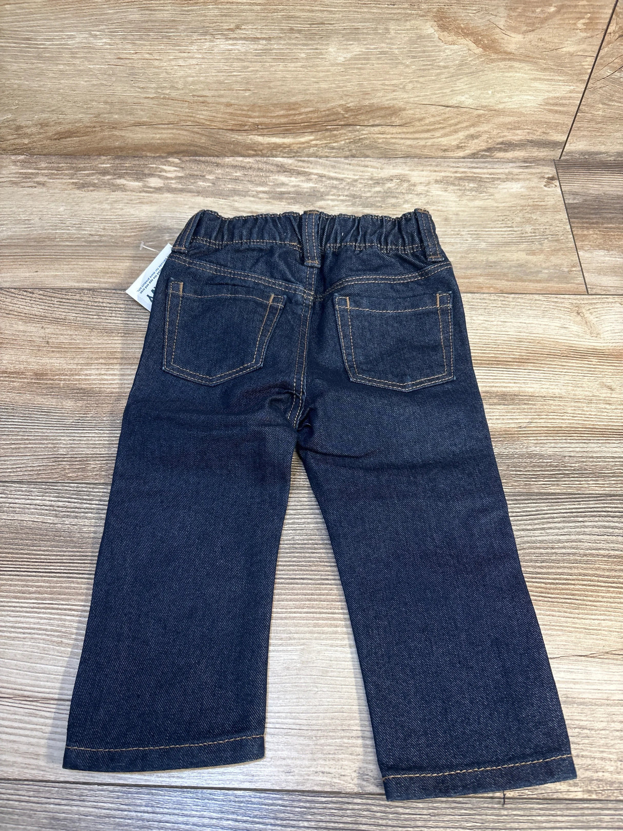 Back view of toddler dark wash denim jeans with elastic waistband and back pockets on wood floor