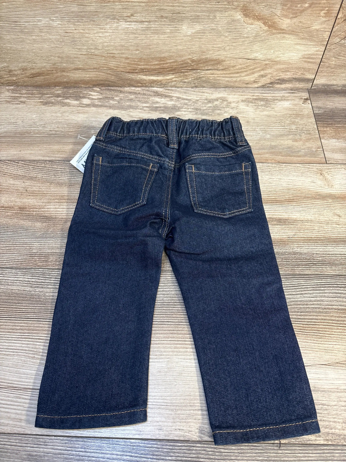 Back view of toddler dark wash denim jeans with elastic waistband and back pockets on wood floor