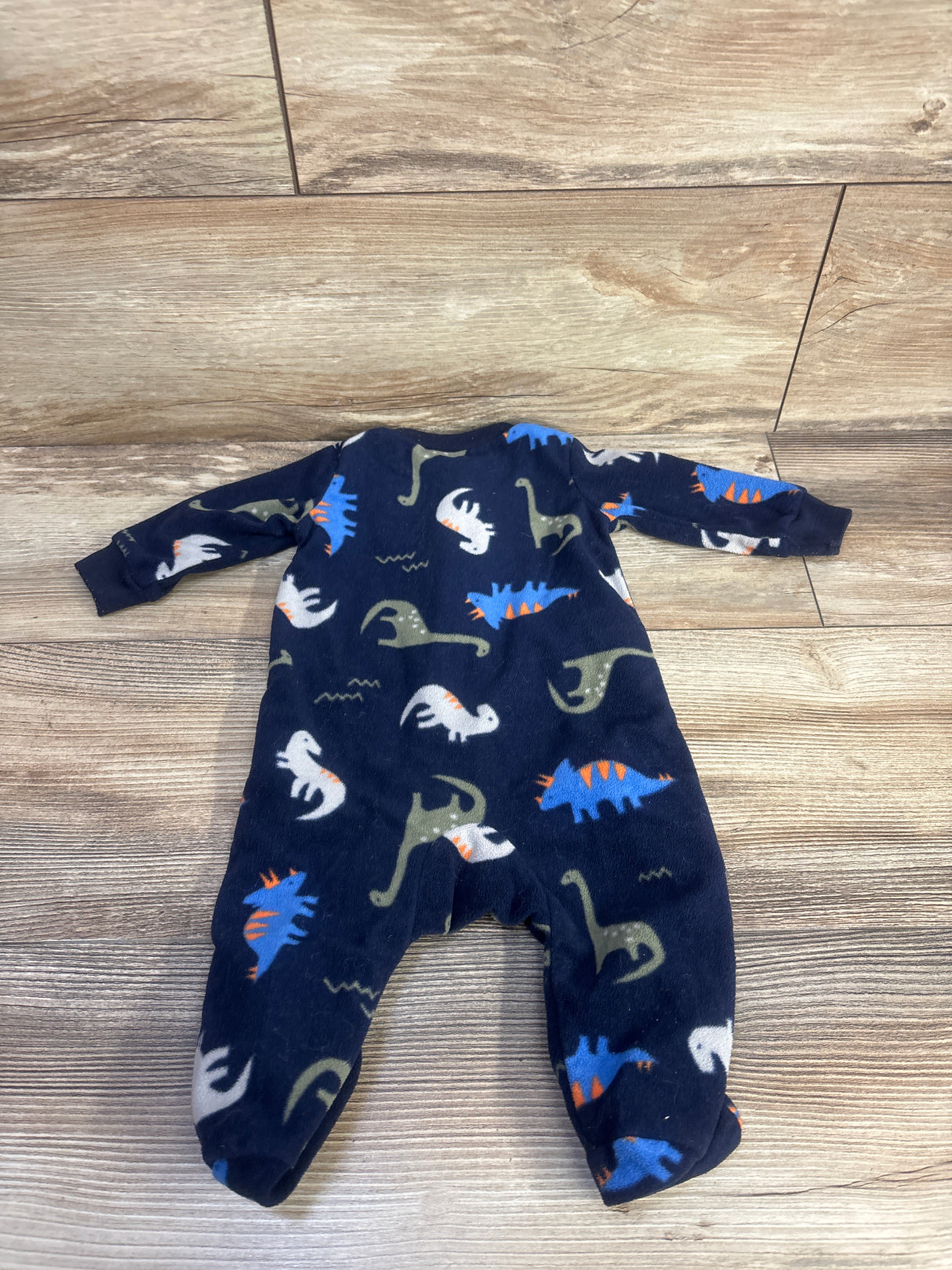 Flat lay of Simple Joys navy baby blanket sleeper showing all-over multicolored dinosaur print on wood floor background
