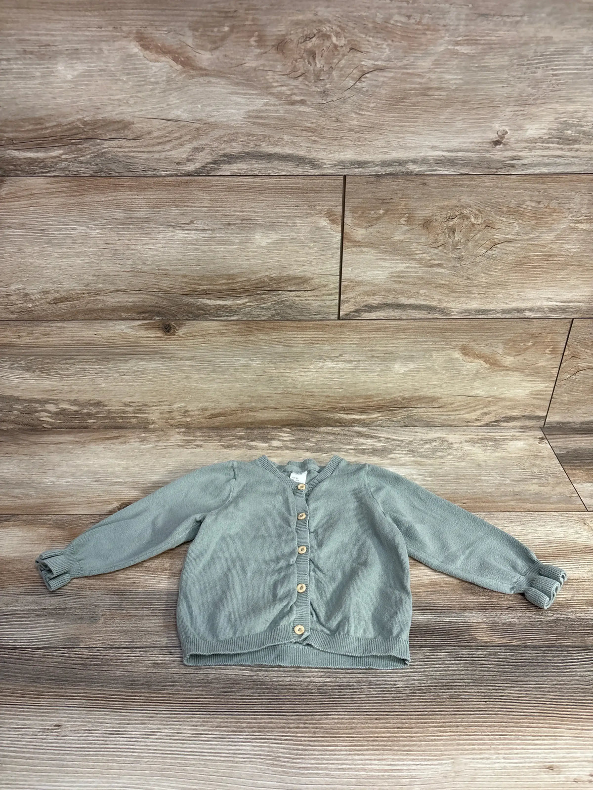 Light green baby cardigan with wooden buttons on wooden floor background