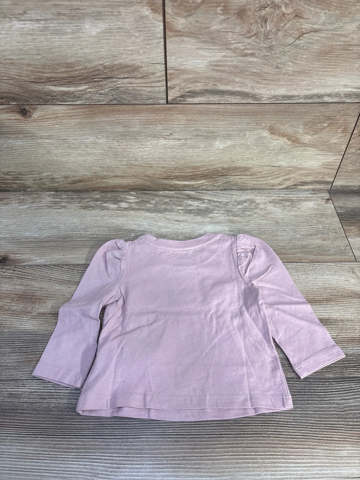 Front view of pink Baby Gap ballerina long sleeve shirt showcasing puff sleeves, laid flat on wood-look flooring