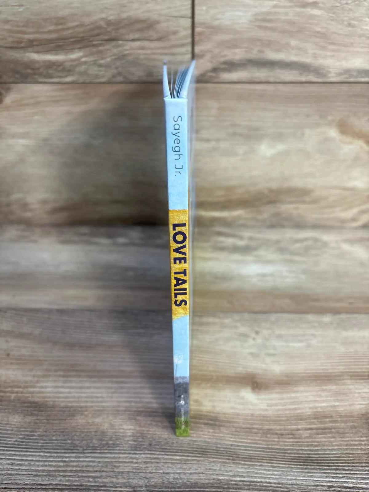 Spine view of Love Tails Hardcover Book showcasing blue cover and yellow LOVE TAILS lettering with a wood-grain background