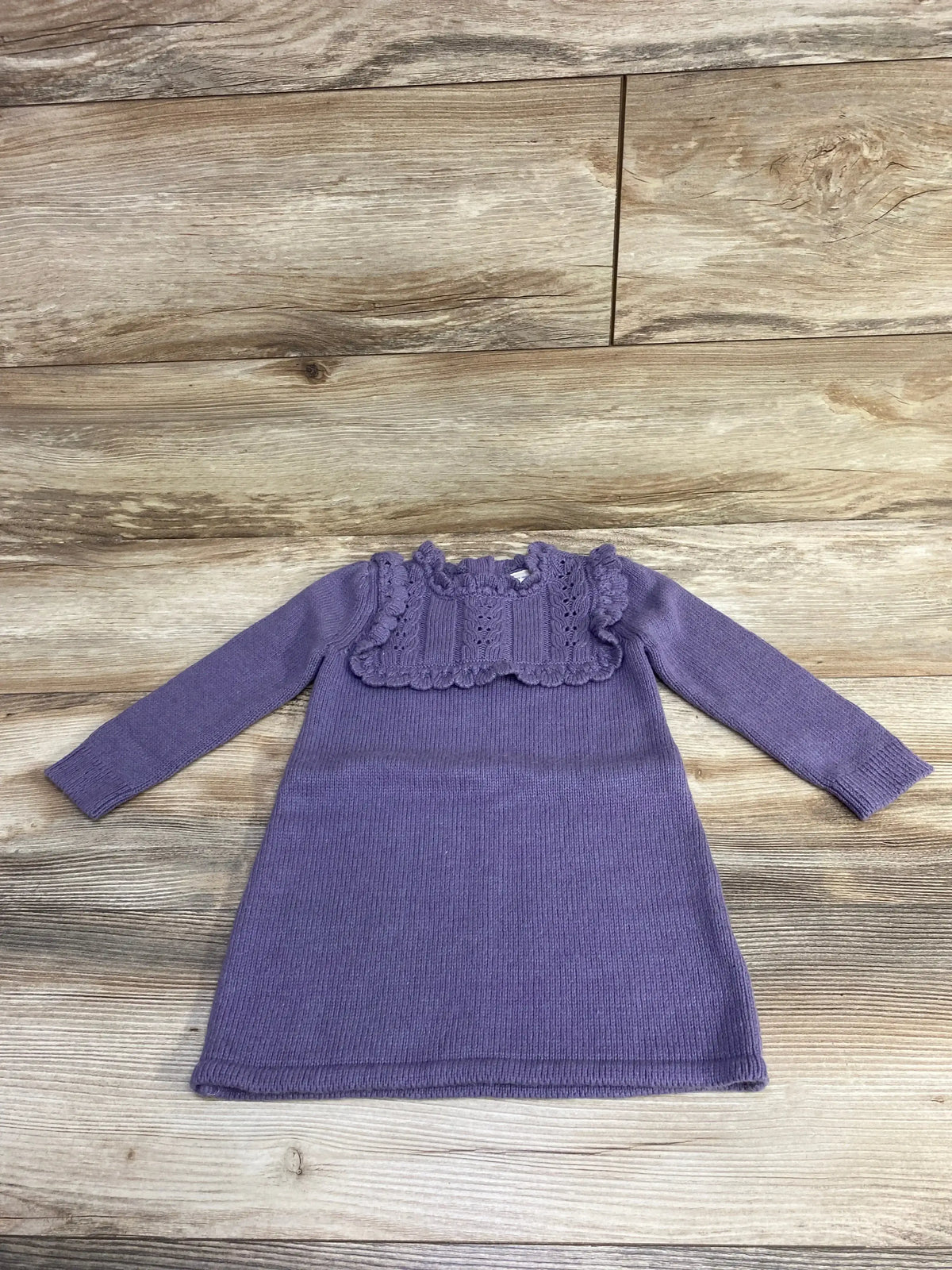 Purple knitted long sleeve baby dress with ruffled lace detail on wooden background