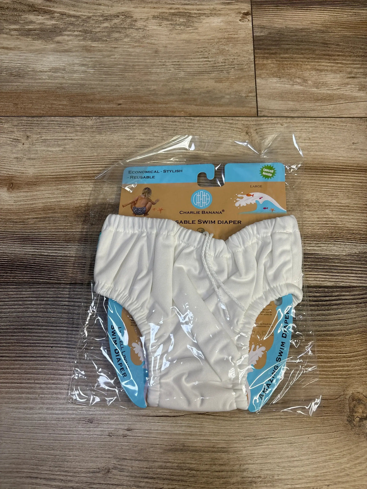 Front view of Charlie Banana reusable drawstring swim diaper white with elastic leg openings and drawstring waistband on wood tabletop
