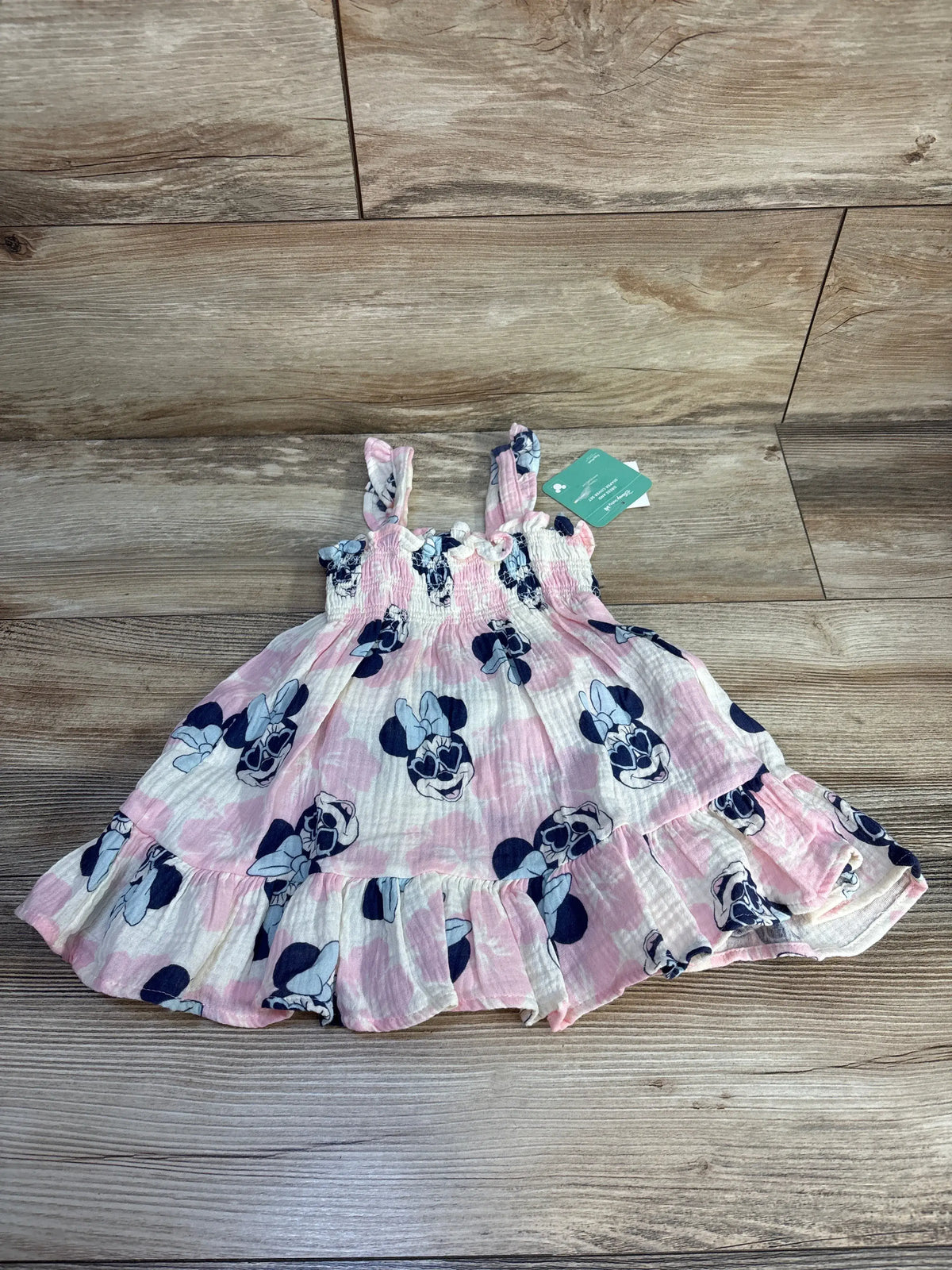 Flat lay of a pink Minnie Mouse smocked gauze dress with smocked bodice and ruffled hem on a wood floor