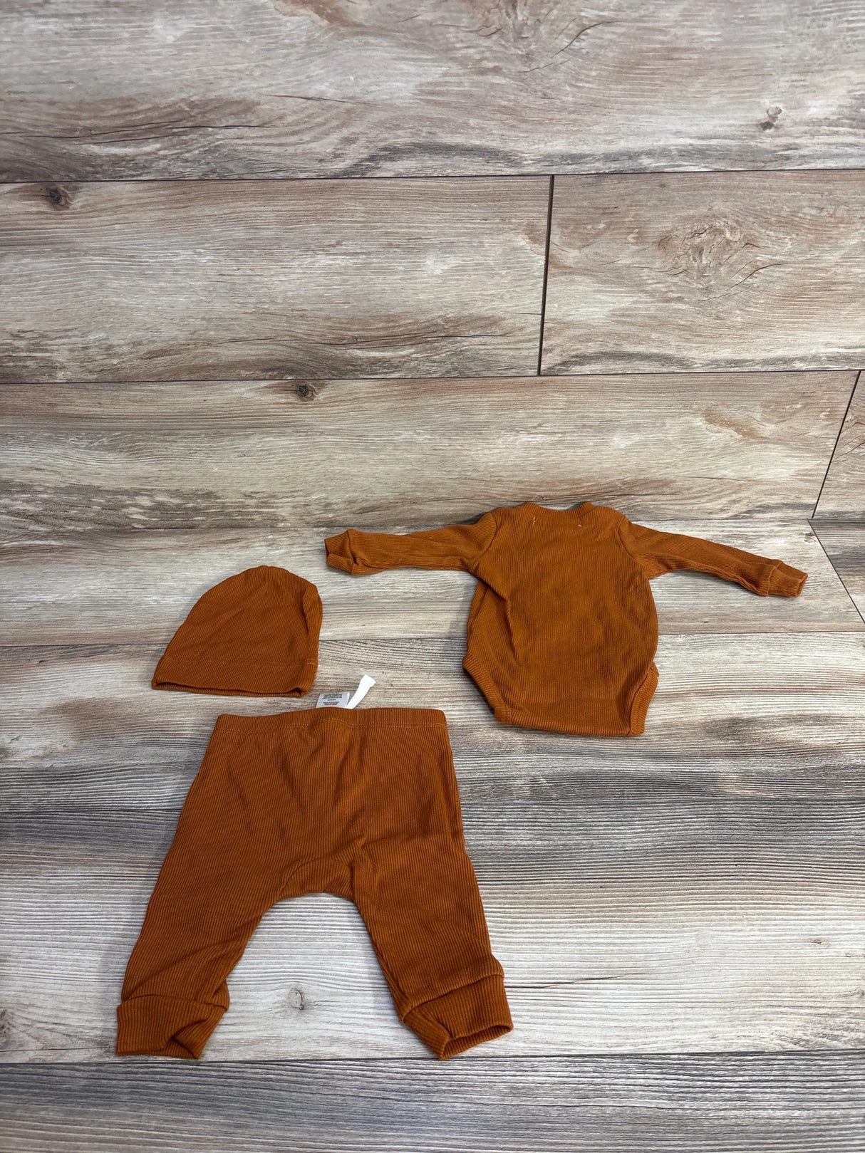 Rust orange ribbed baby outfit set with hat, long sleeve onesie, and pants on wood floor