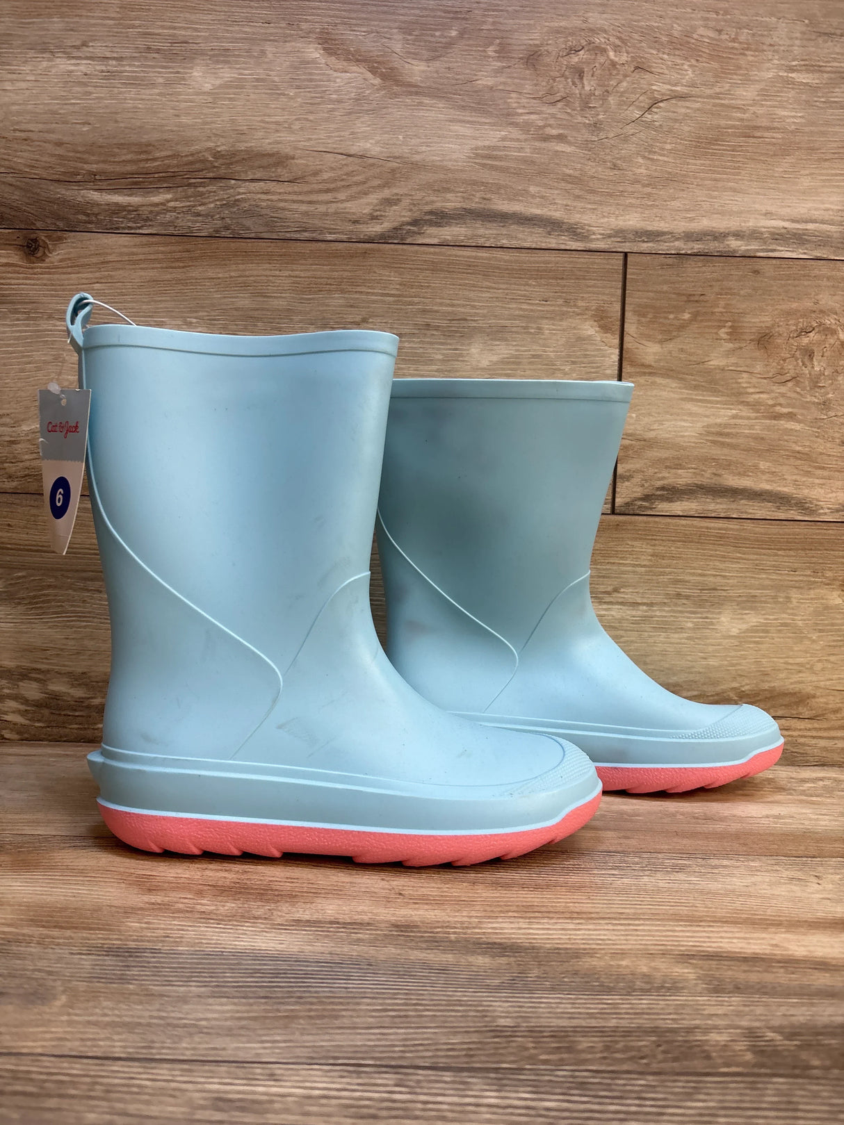 Light blue kids rain boots with pink soles on wooden background, size 6