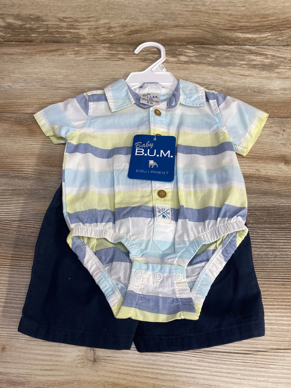 Flat lay of Baby B.U.M. striped bodysuit and navy shorts showcasing collar buttons and snap crotch on wood floor