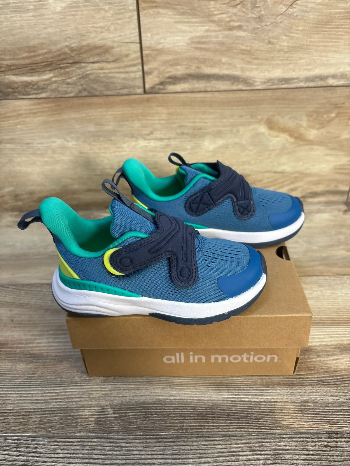 Blue and green toddler athletic sneakers with hook-and-loop straps on a shoebox, wood background
