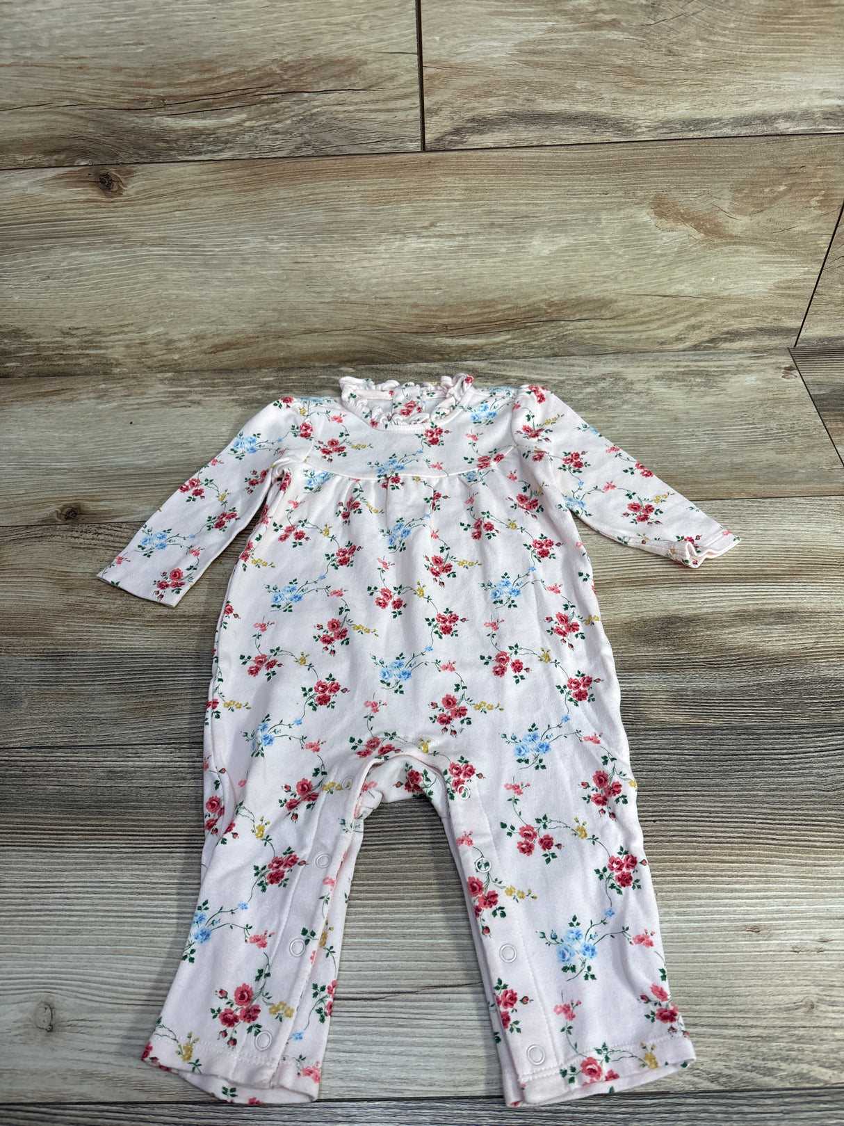 Baby pink floral long-sleeve romper with snap buttons on wooden background