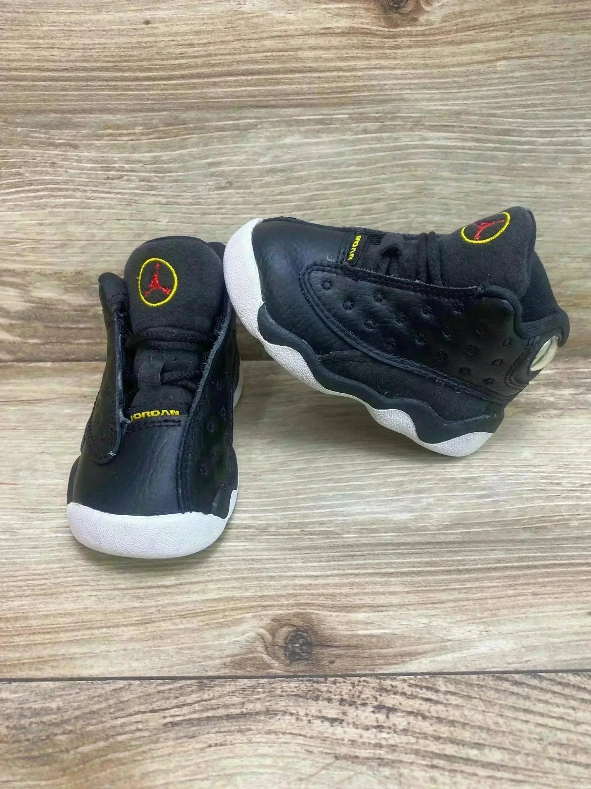 Front and side view of toddler Air Jordan 13 Playoff sneakers, black leather and suede, white soles and red Jumpman on wood