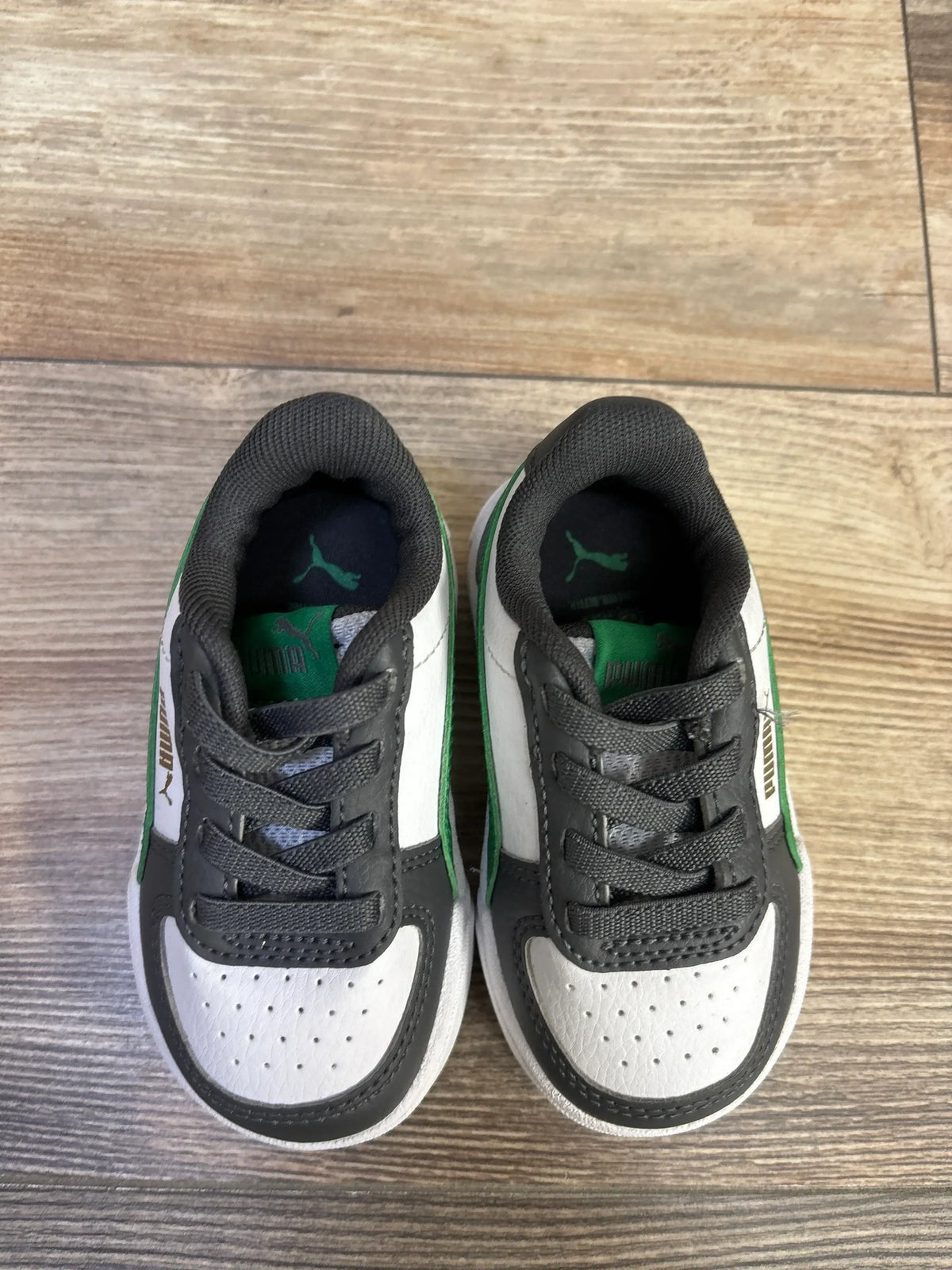 Top-down view of Puma Caven 2.0 toddler sneakers size 5C showing white perforated toe, gray overlays, green accents, and Puma logo on wooden floor