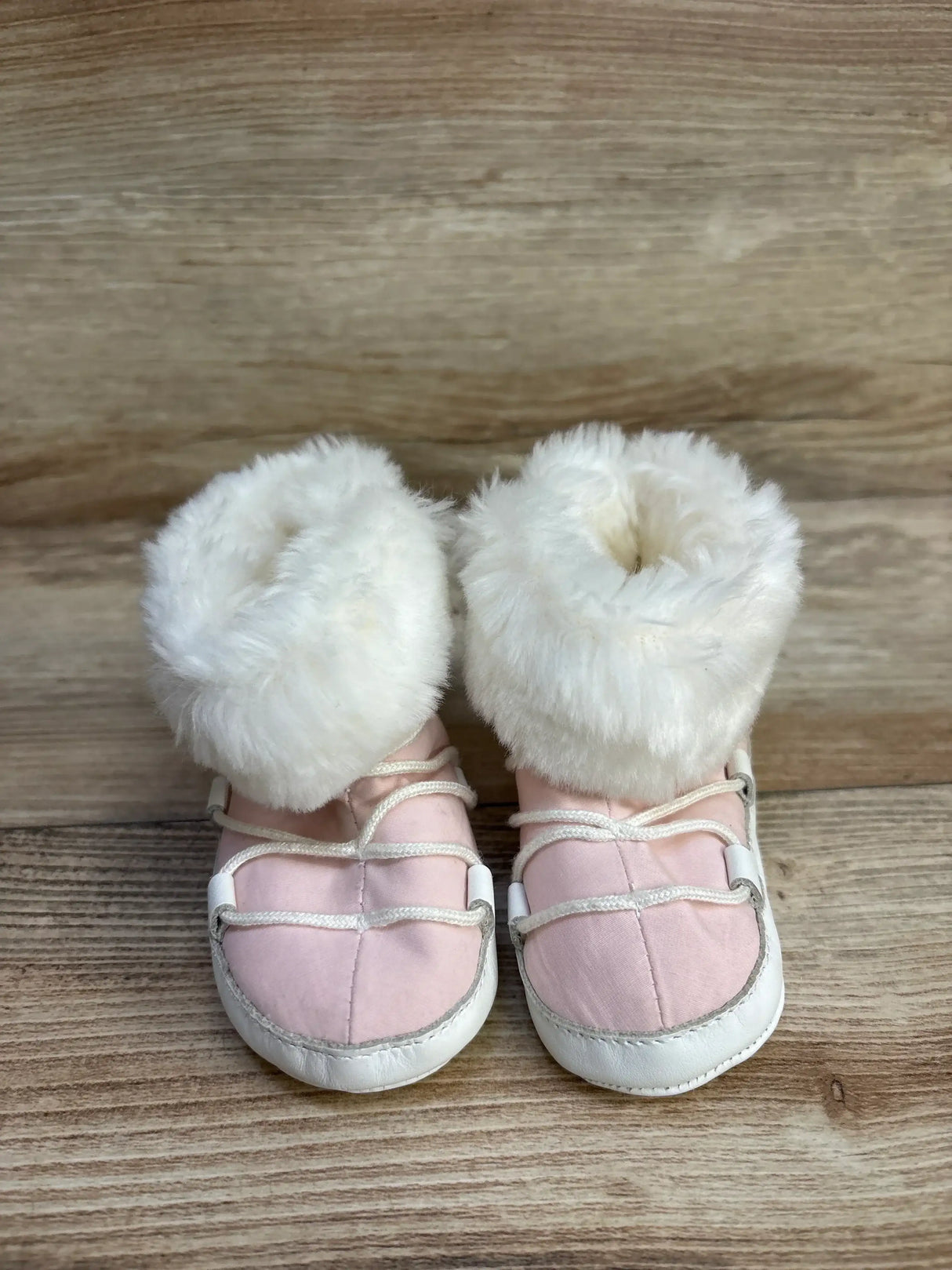 Pink baby booties with white faux fur on a wooden background
