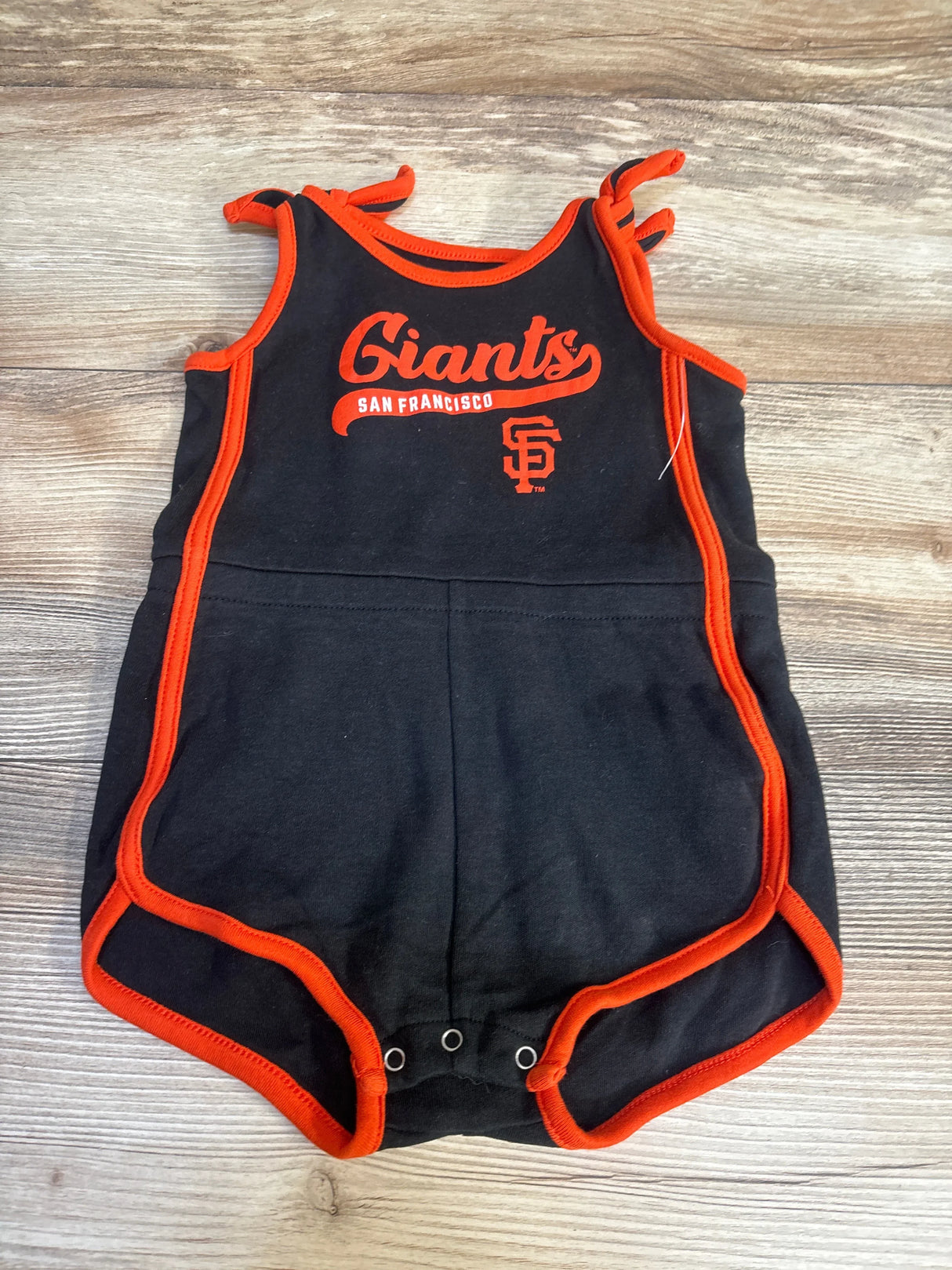 Black and orange San Francisco Giants baby romper with snap closures, on wood background