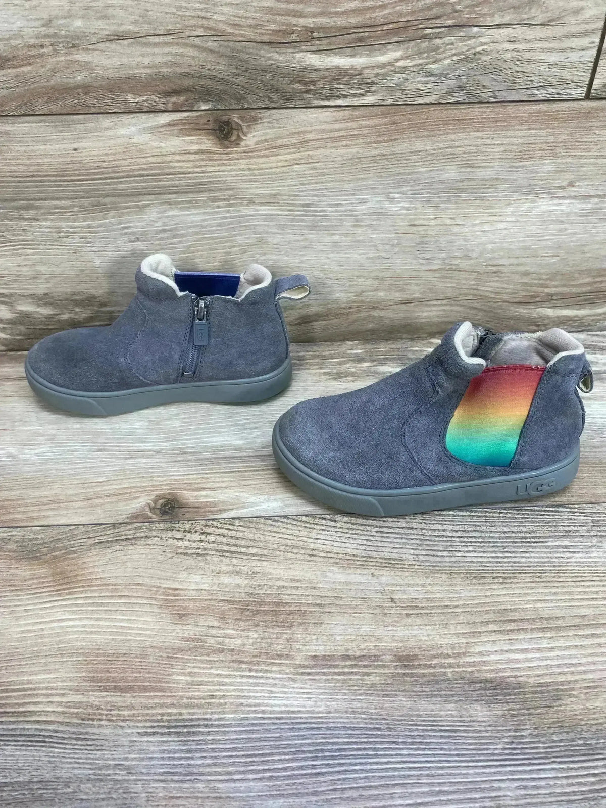 Side view of UGG Hamden II suede toddler sneakers in grey showing rainbow elastic side panel and shearling lining on wood background